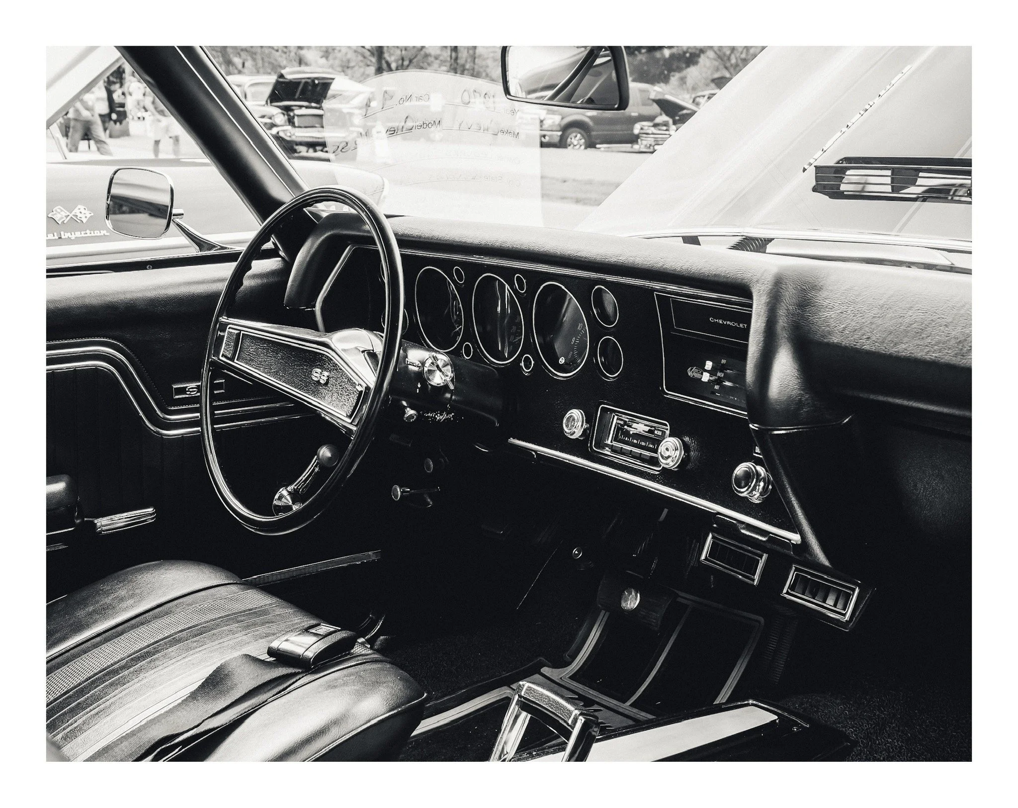 Interior of a vintage Chevrolet car, showing the steering wheel, dashboard with gauges, and seating in black and white.