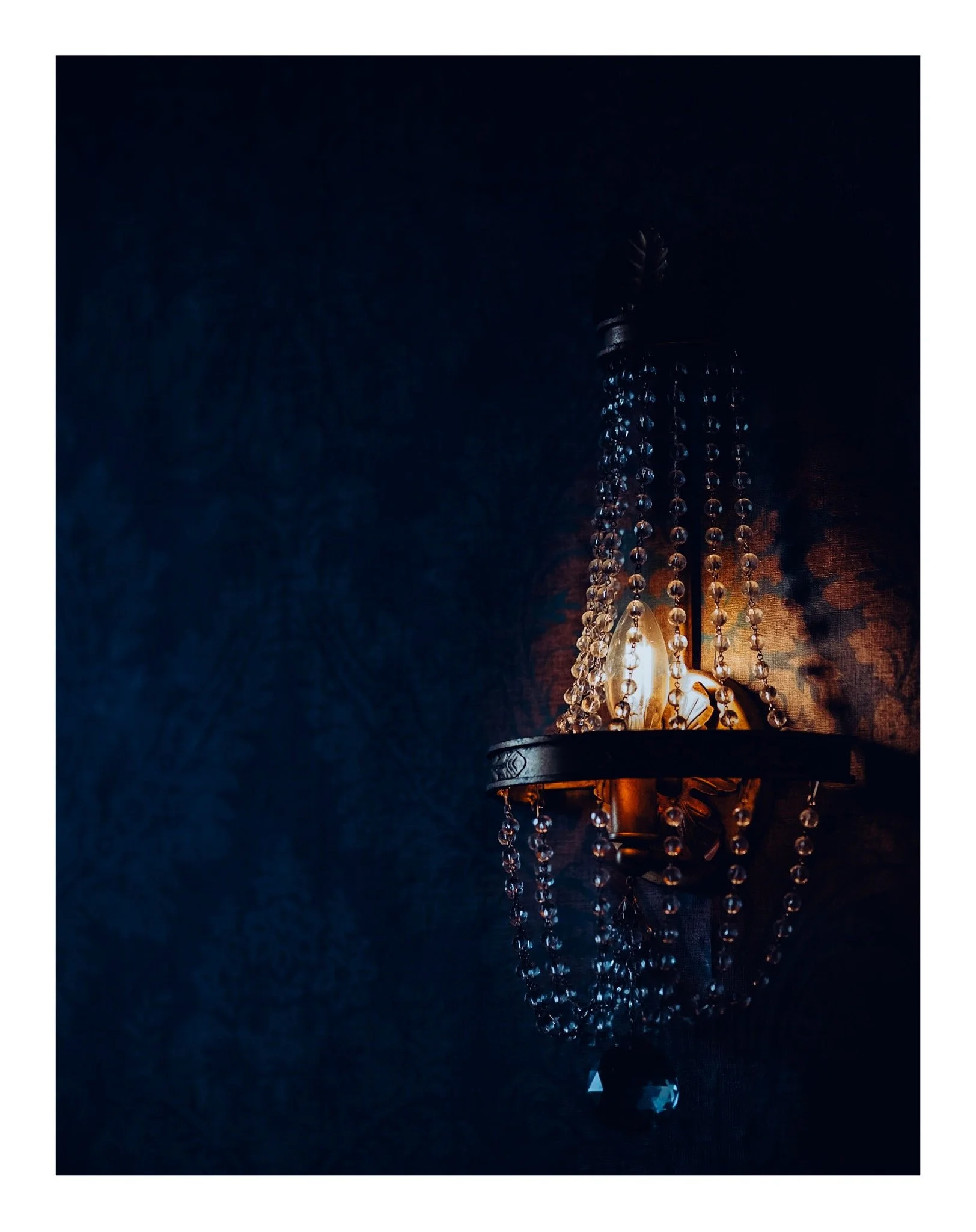 A close-up view of a chandelier with hanging crystals, illuminated in a dark setting.