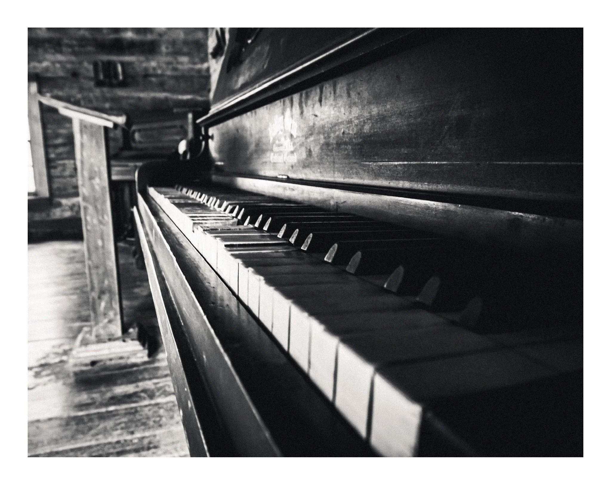 Black and white photo of a vintage piano with keys and wooden surface, in a rustic setting.
