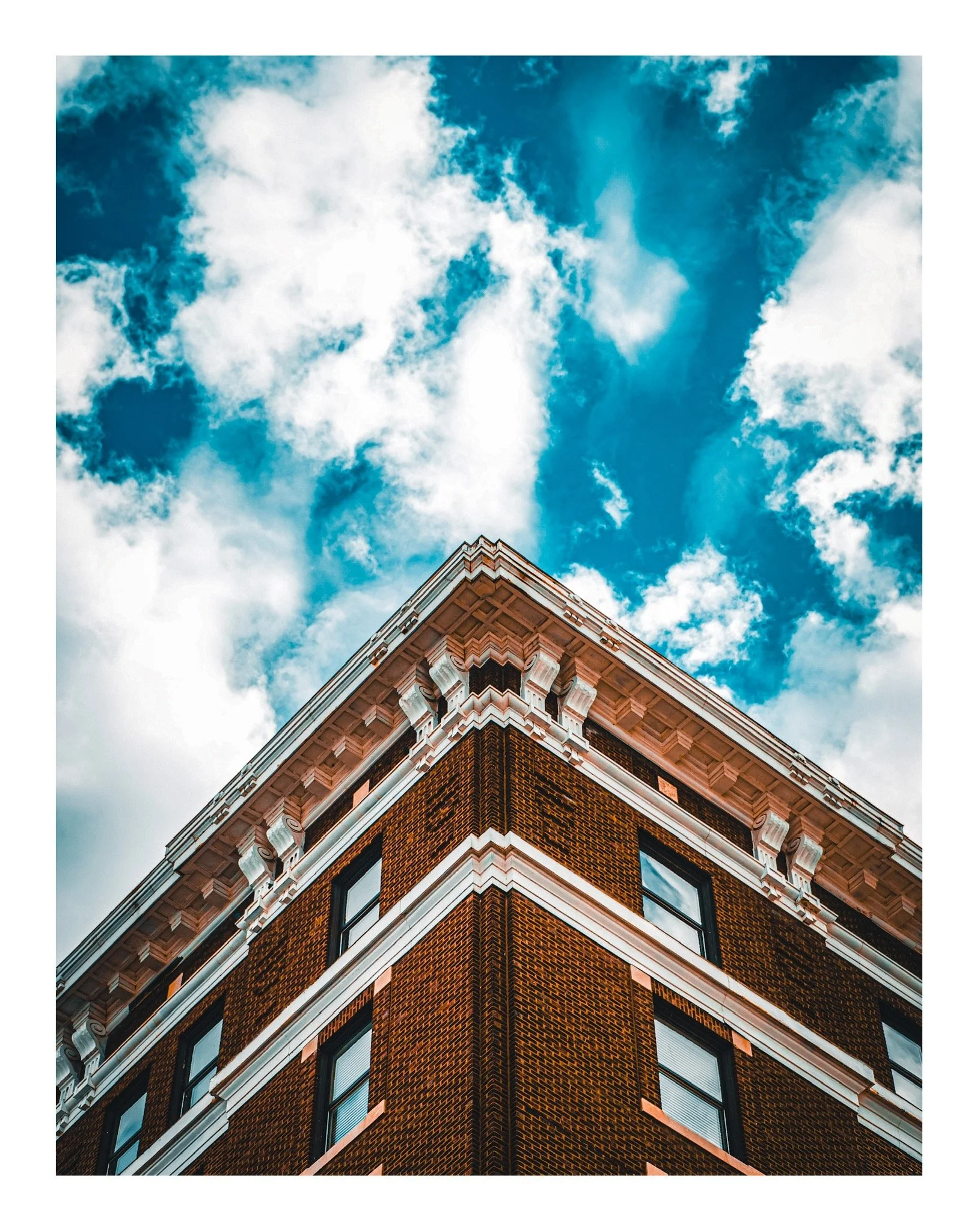 Low-angle view of a corner of a brick building with ornate white decorative trim, set against a bright blue sky with scattered clouds.
