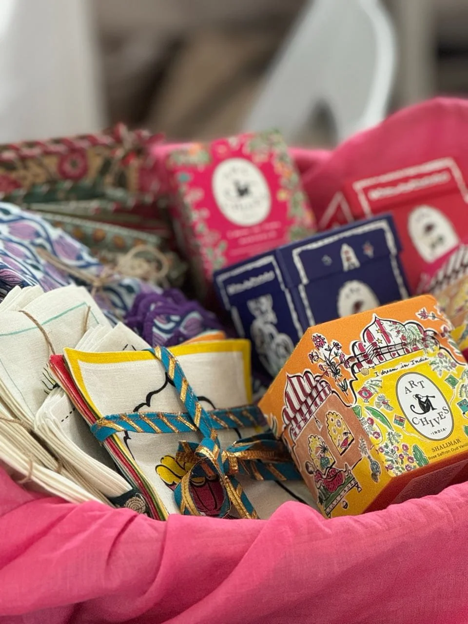Colorful packages of tea, including Art Chives tea, wrapped in decorative paper and tied with strings, displayed on a pink fabric surface.