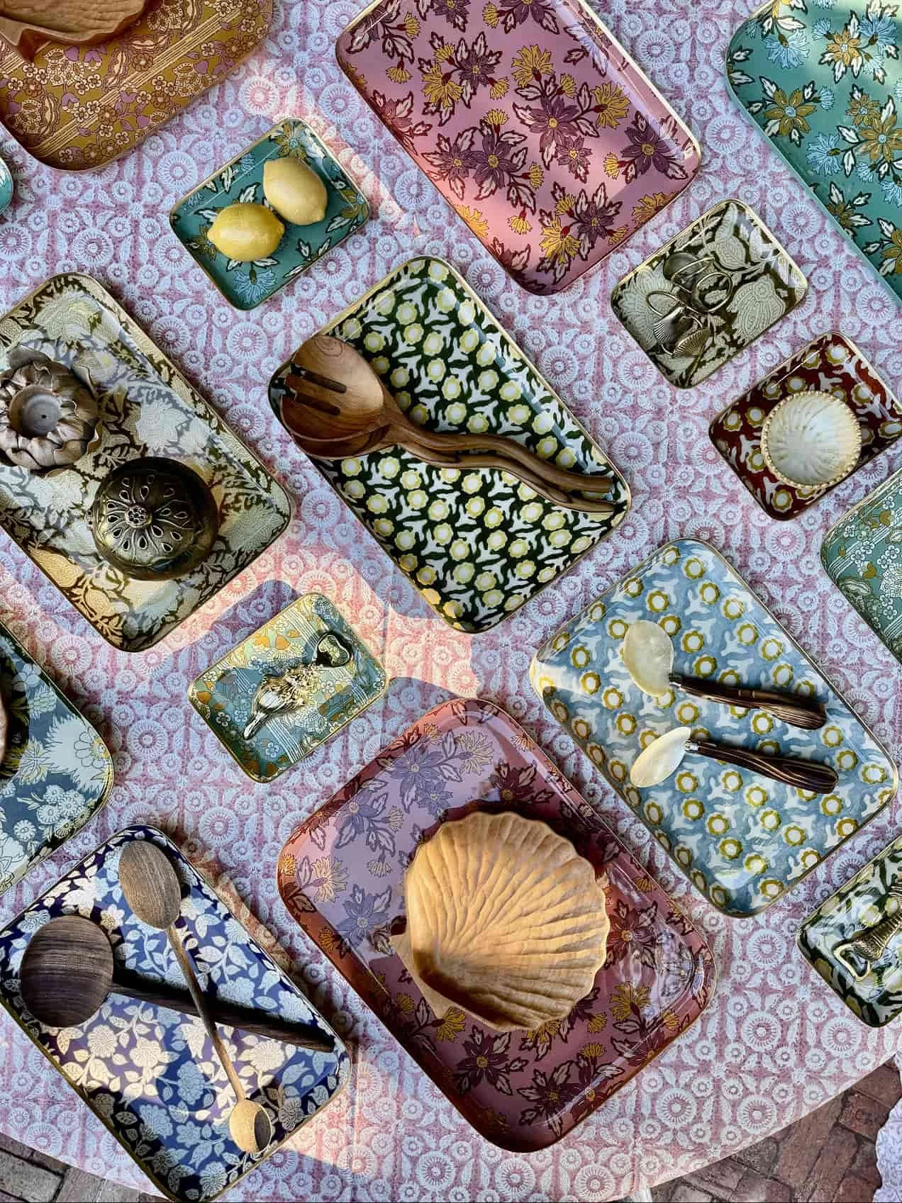 Colorful decorative trays with seashells, lemons, and wooden utensils on a pink patterned tablecloth.