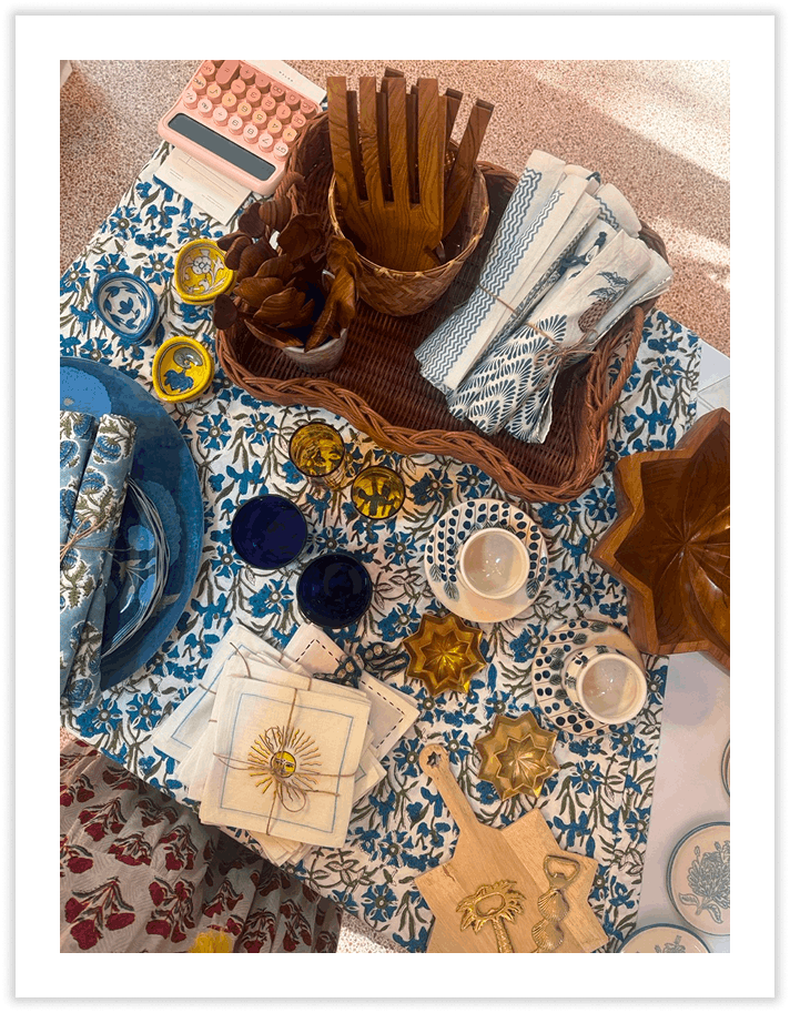 Table set with dishes, napkins, decorative candles, and utensils, including a pink box of makeup, a basket with napkins and wood utensils, and various decorative items like star-shaped bowls and jewelry.