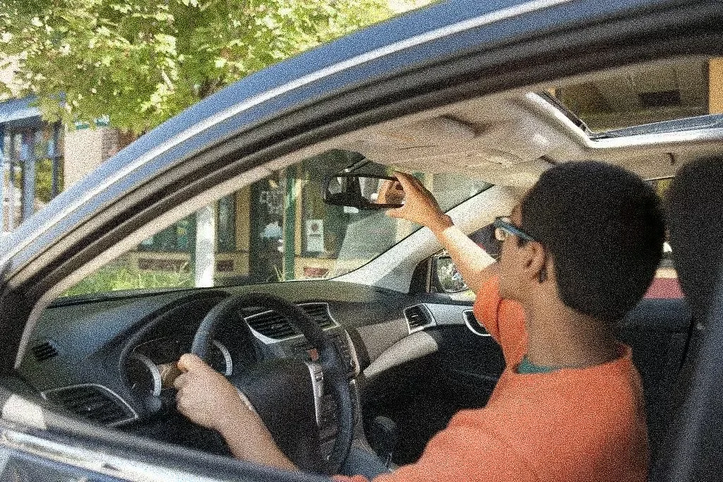 Un niño con gafas sentando en el asiento del conductor de un automóvil, tomando una selfie con su teléfono celular