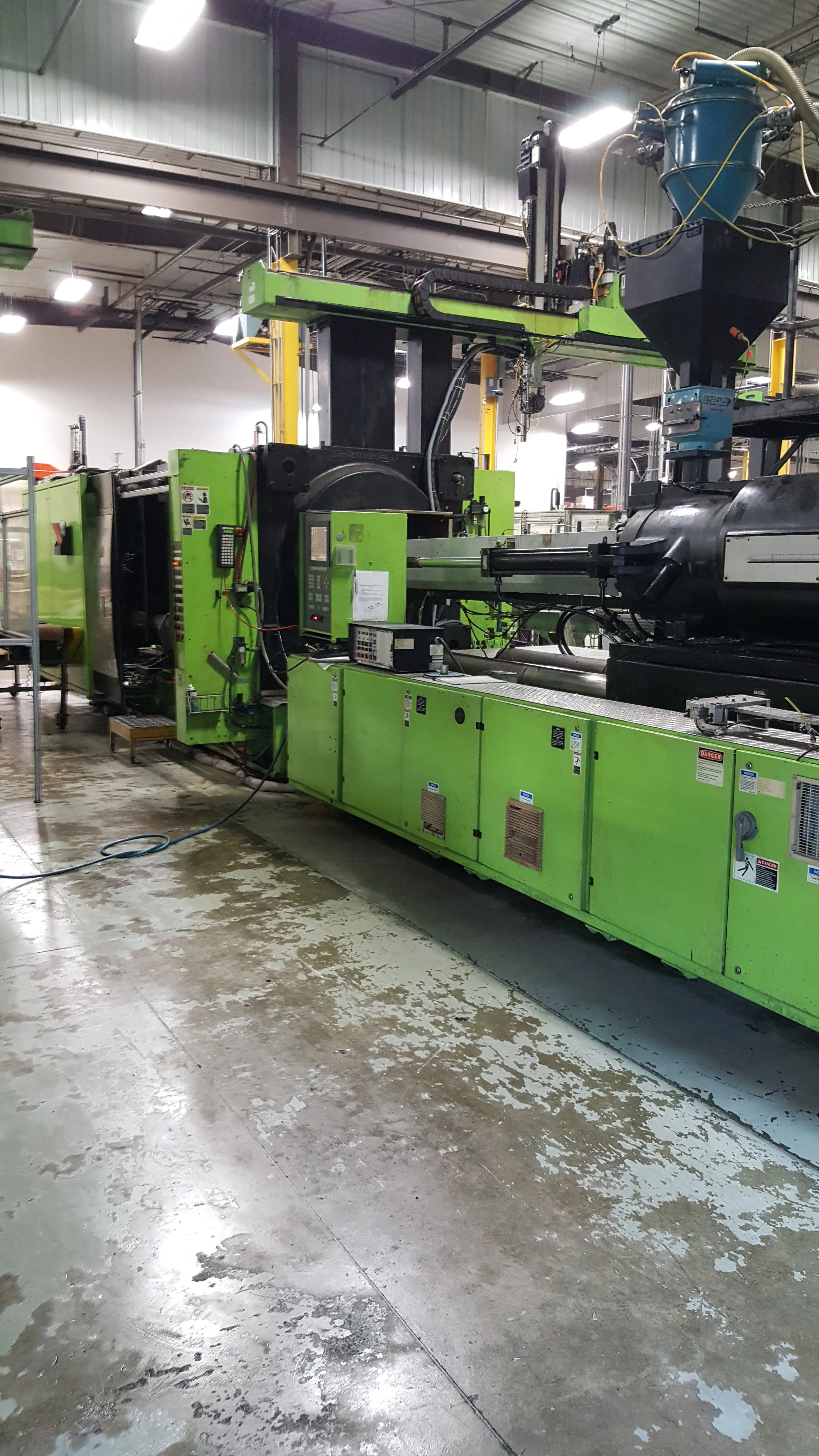 Large industrial plastic molding machine in a factory setting with a concrete floor.
