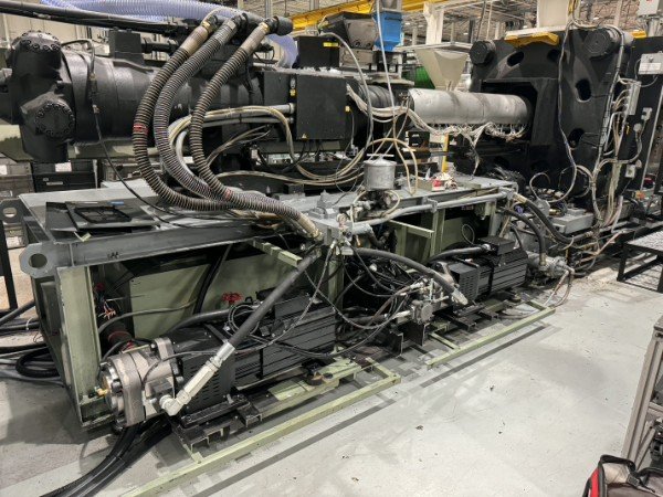 A complex piece of machinery with numerous black cables, pipes, and metal components, likely part of industrial equipment or manufacturing machinery.
