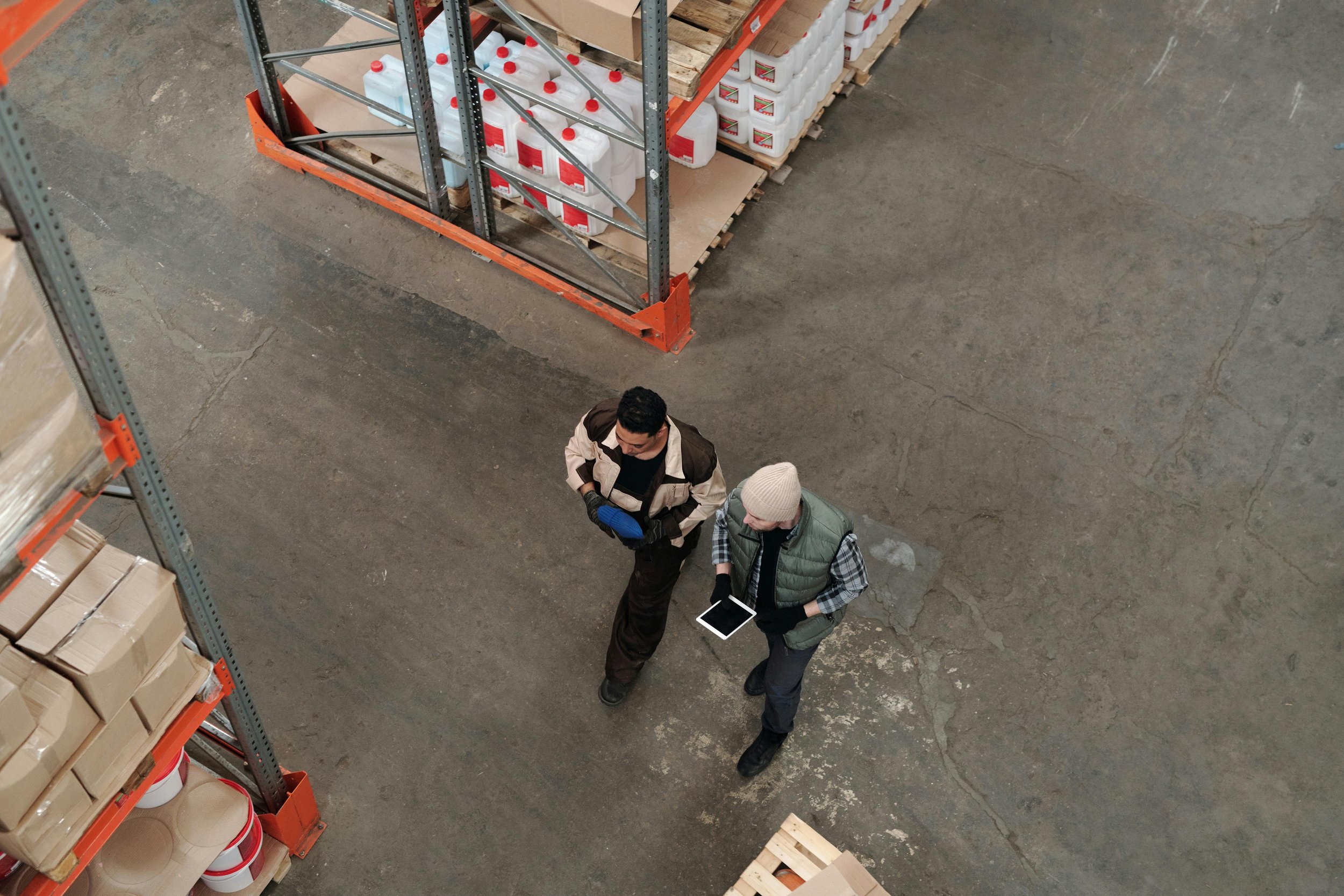 Two people talking in a warehouse aisle, with shelves of boxes and supplies around them.