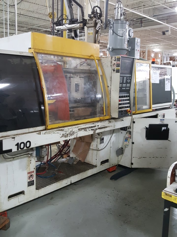 Industrial manufacturing machine with a yellow safety cover and control panel inside a factory setting.