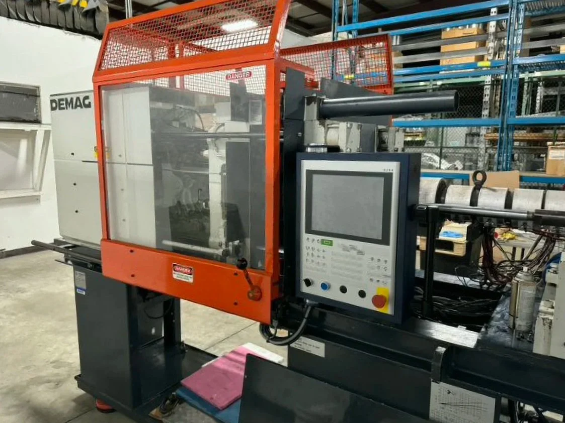 Industrial machine with a control panel in a warehouse setting, surrounded by shelves and miscellaneous equipment.