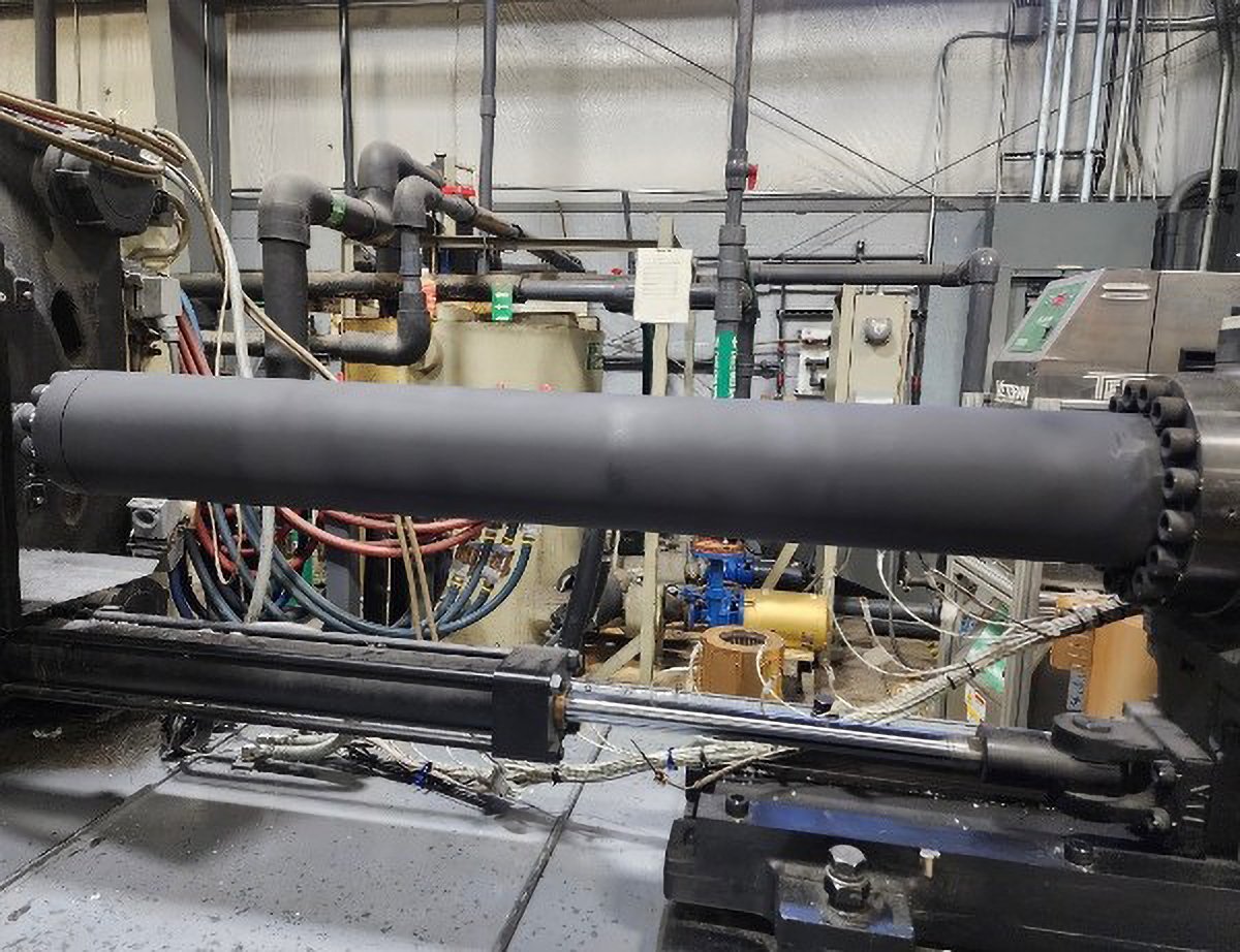 Industrial machinery with a large black cylindrical component, various pipes, wires, and control panels in a factory setting.