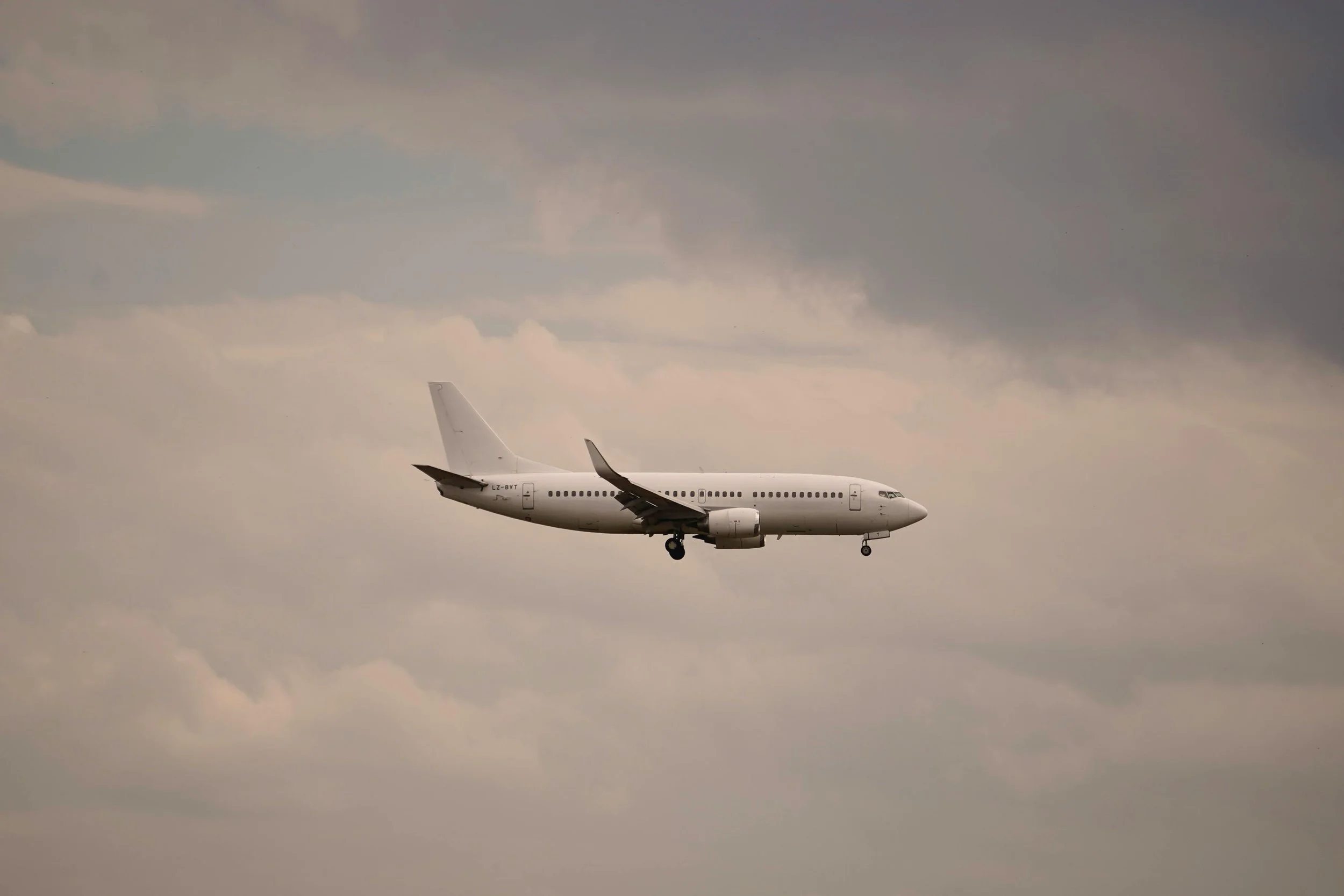 A white commercial airplane flying through a cloudy sky with its landing gear extended.