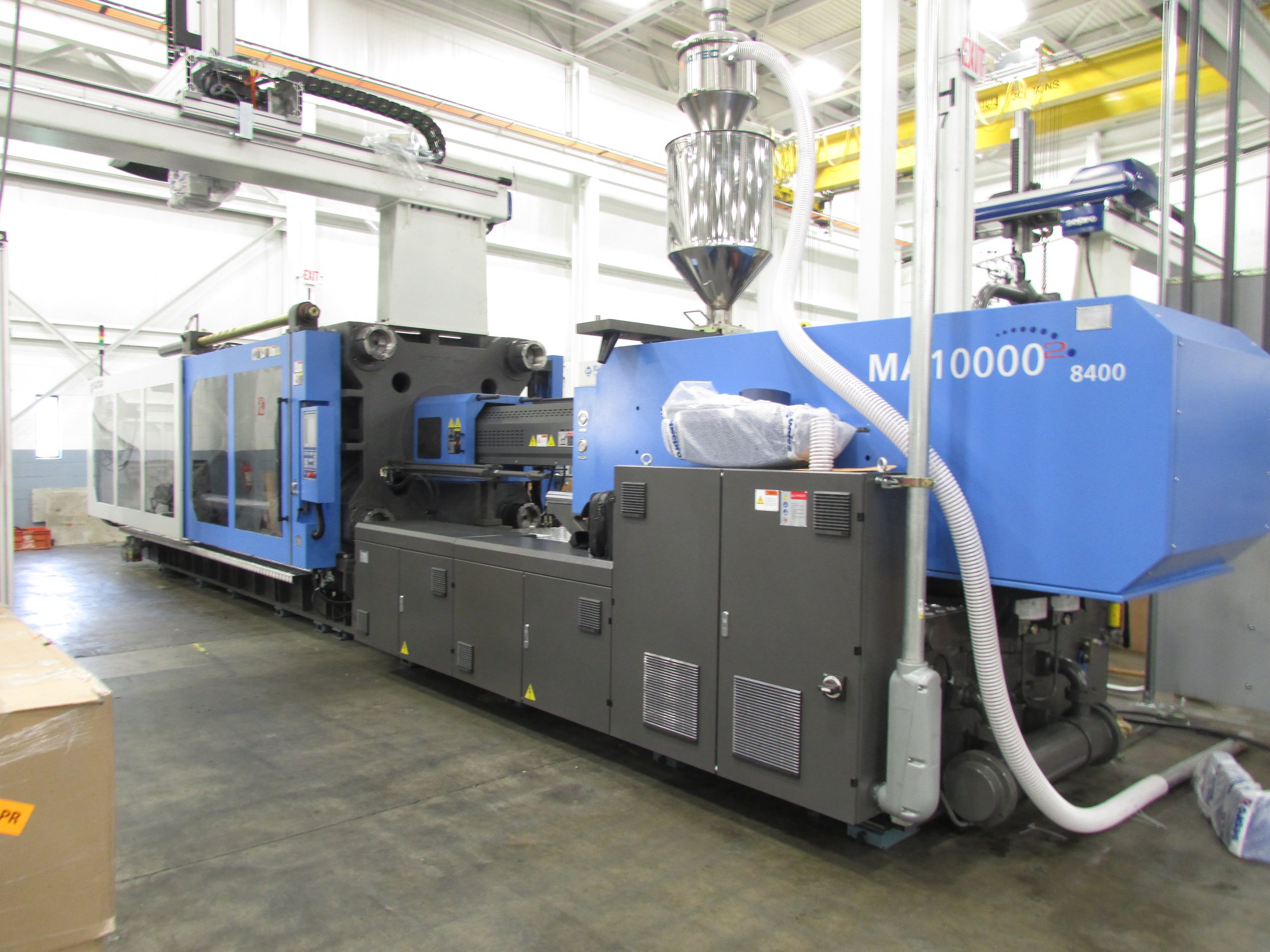 Industrial machinery in a factory setting, with large blue and black components, pipes, and mechanical parts visible.