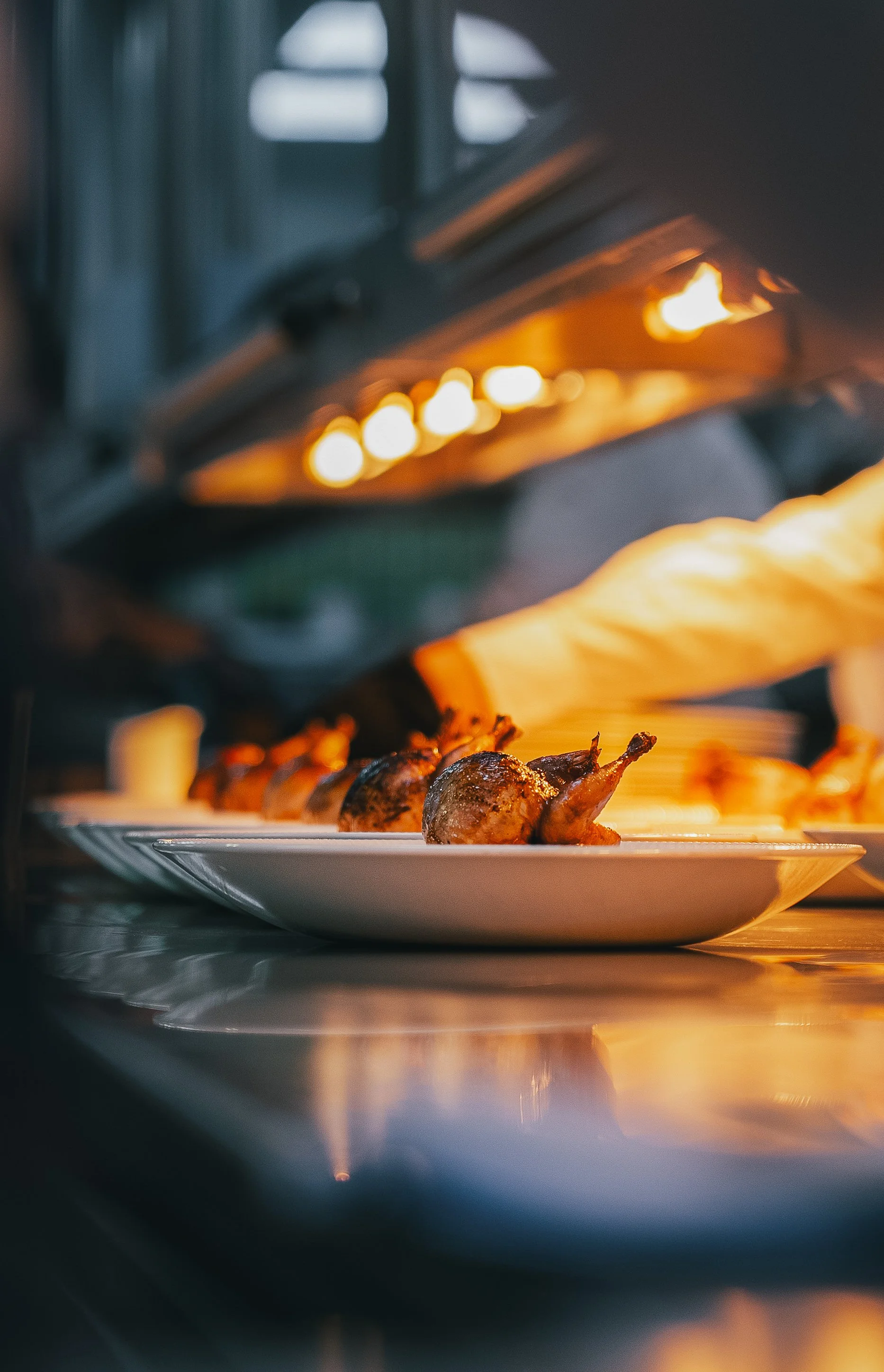 Close-up of chicken drumsticks cooking on a white plate inside an oven with warm light.