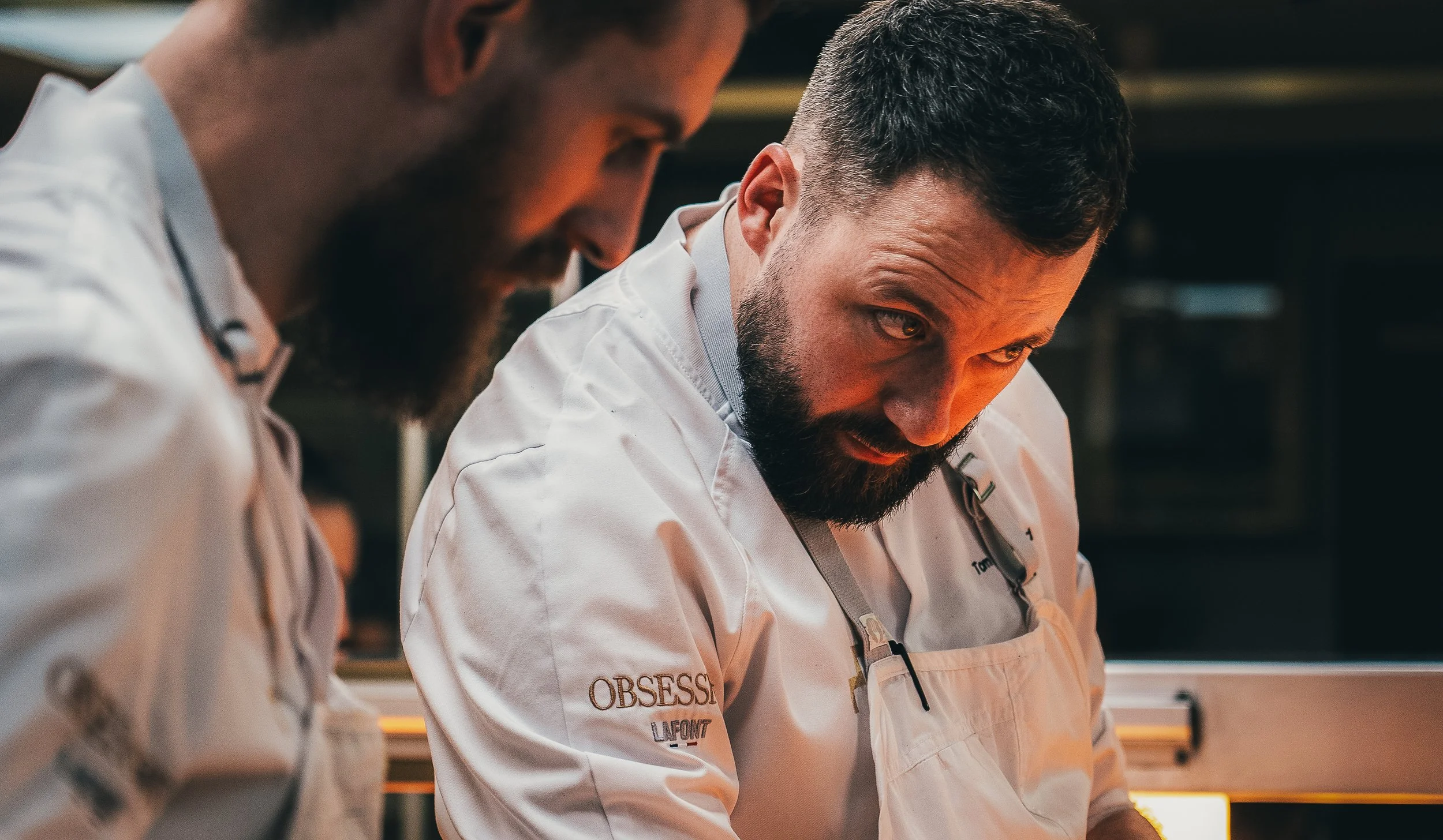 Two male chefs in white uniforms focused on preparing food in a professional kitchen.
