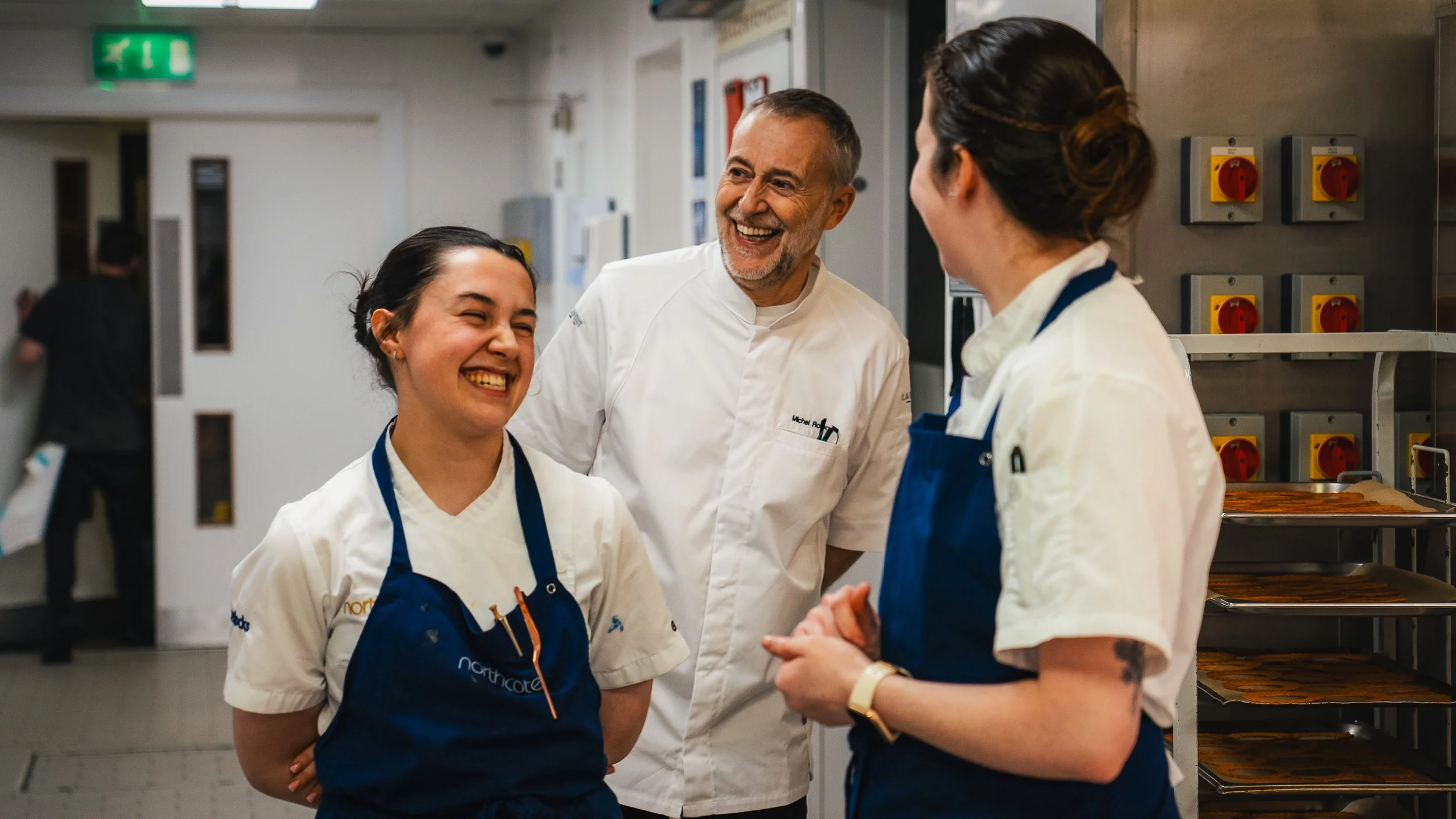 Chef and kitchen staff smiling and talking in a professional kitchen.