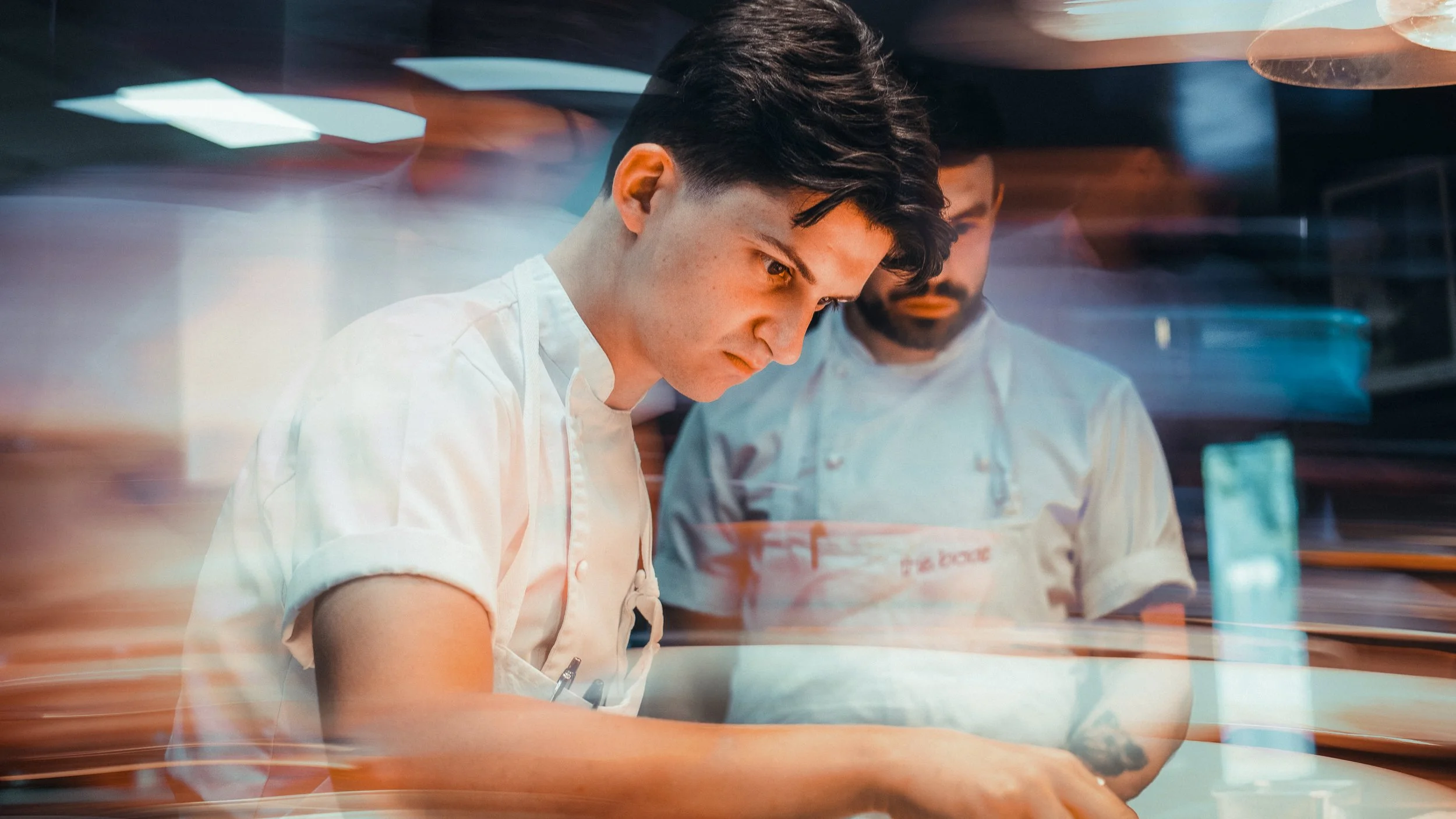 Two chefs working in a busy kitchen, focusing on preparing food.