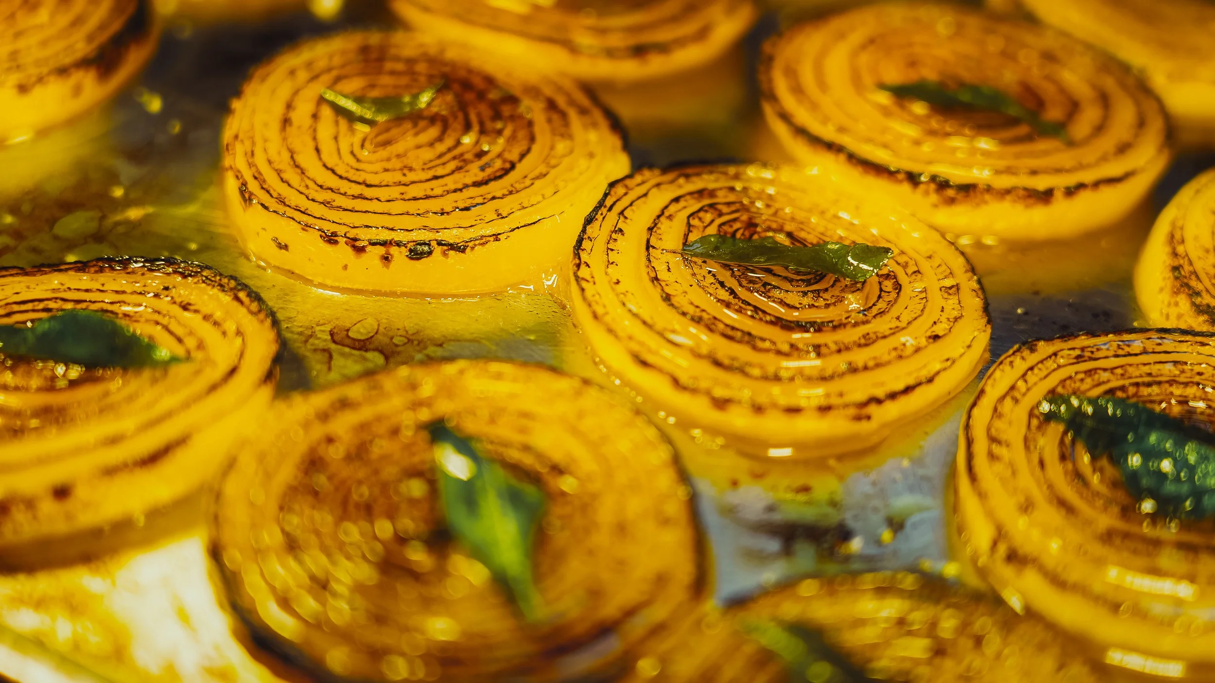 Close-up of yellow and black spiral-patterned sweets garnished with green leaves, cooking in oil.