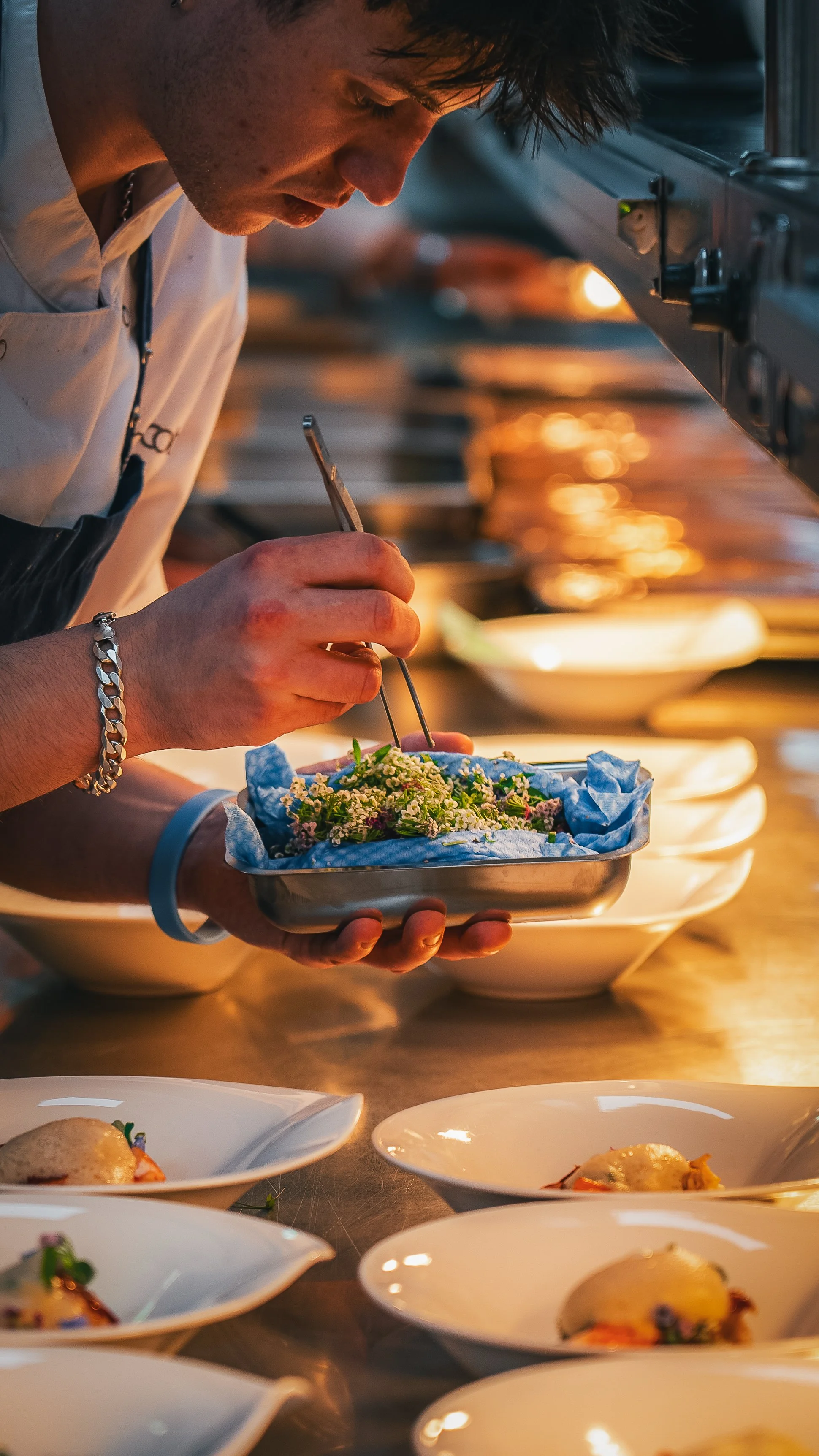 A chef decorates a dish with flowers in a professional kitchen during dinner service.