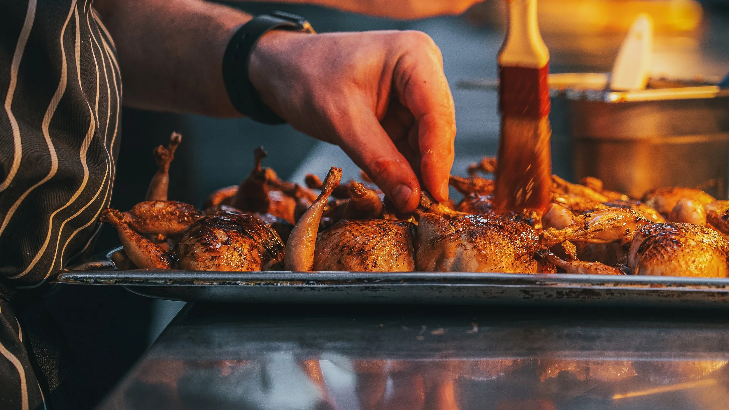 Person grilling seasoned chicken and sausage on a barbecue grill.