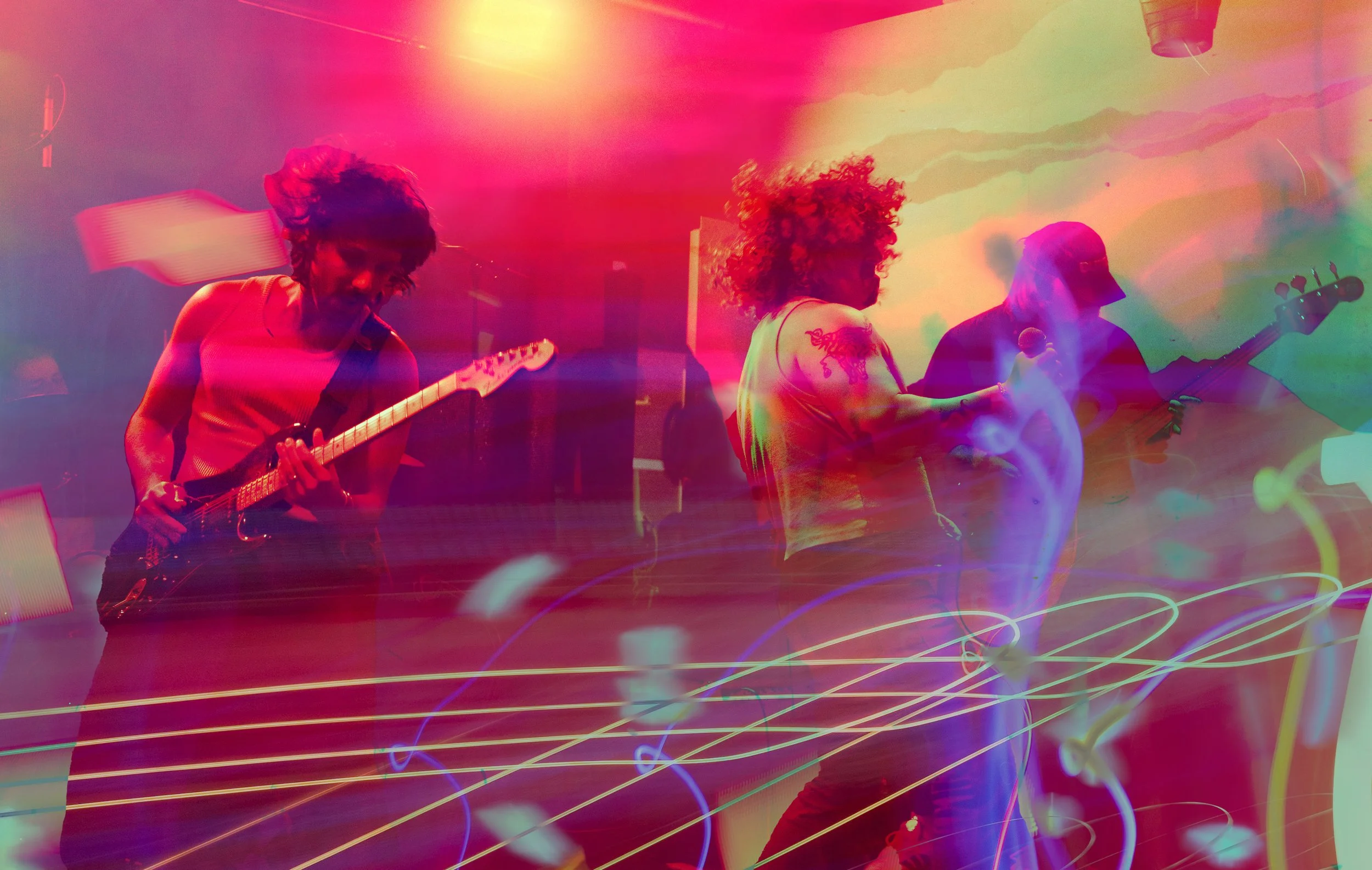 A band of three musicians playing instruments on stage with colorful, blurred lights creating an abstract background.