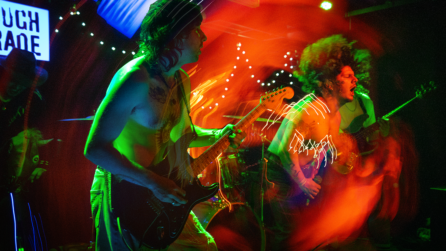 A band performing on stage with colorful stage lighting, featuring guitarists and a singer in a lively concert setting with motion blur effects.