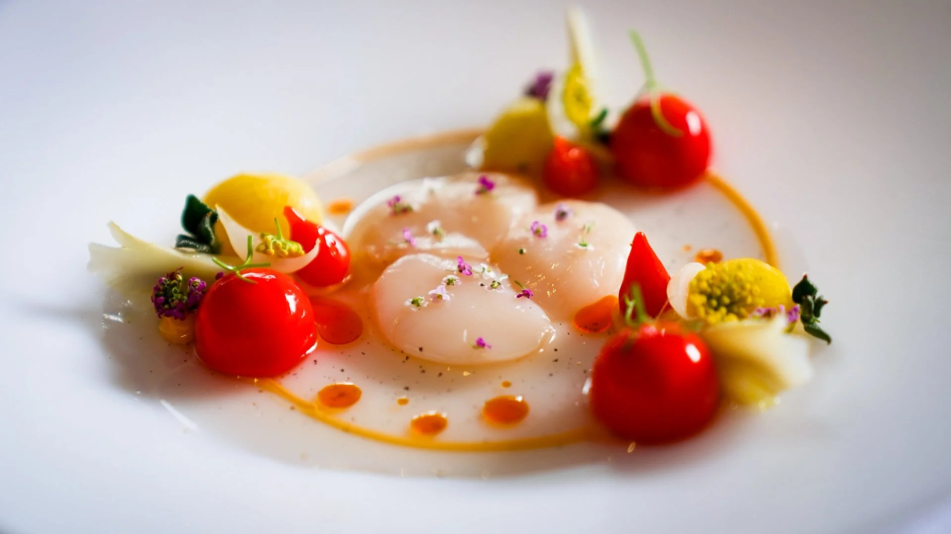 Gourmet dish with white fish, cherry tomatoes, edible flowers, and sauce on a white plate