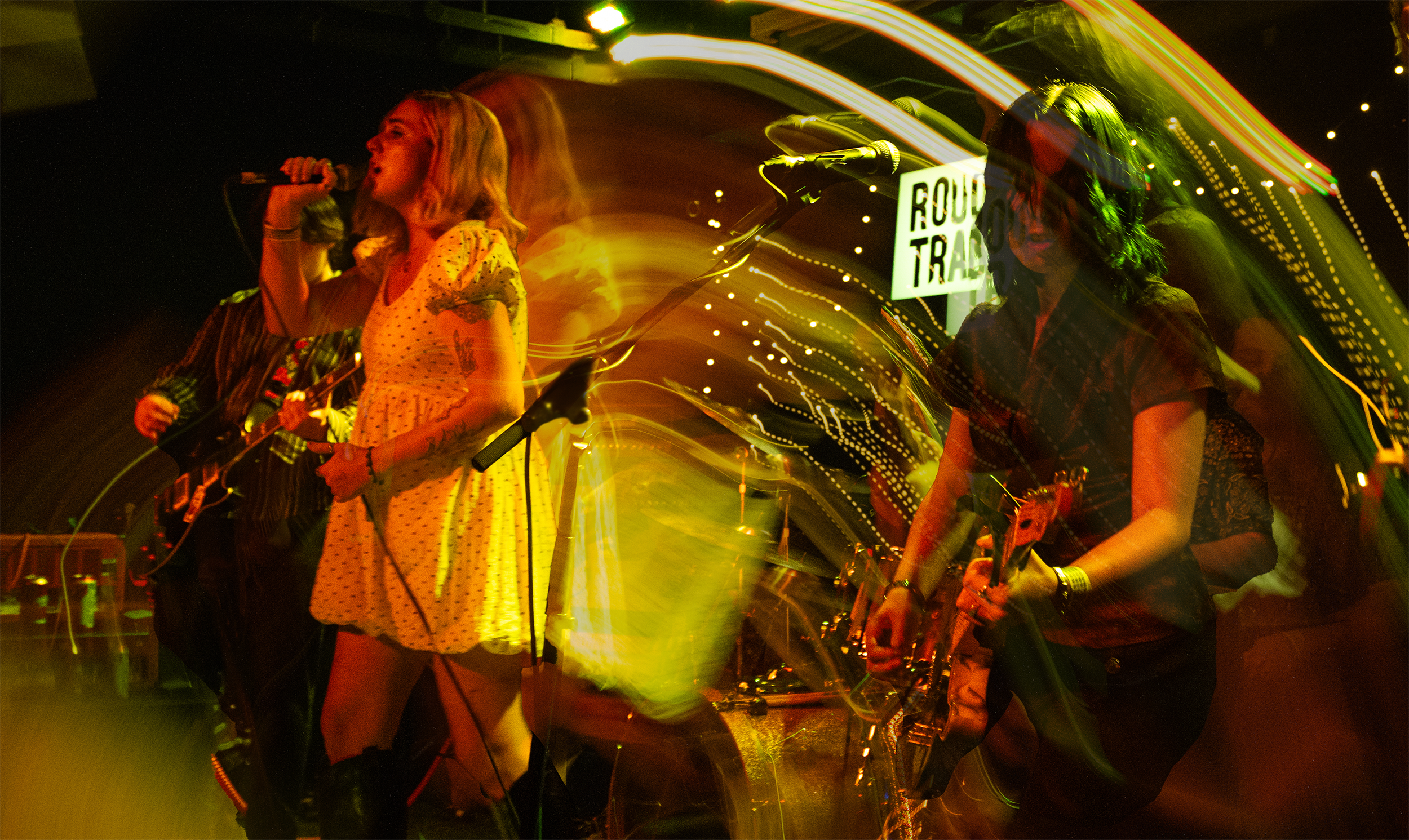 Two women singing and playing guitars with colorful streaks of light in the background at a concert.