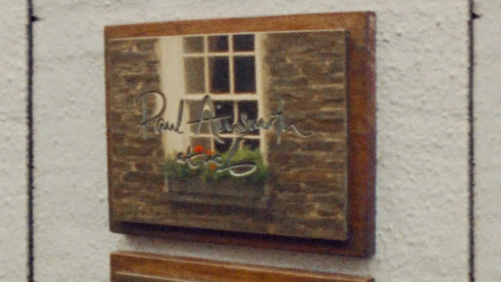 Decorative wooden plaque with mirror reflecting a window and wall, mounted on a textured wall.