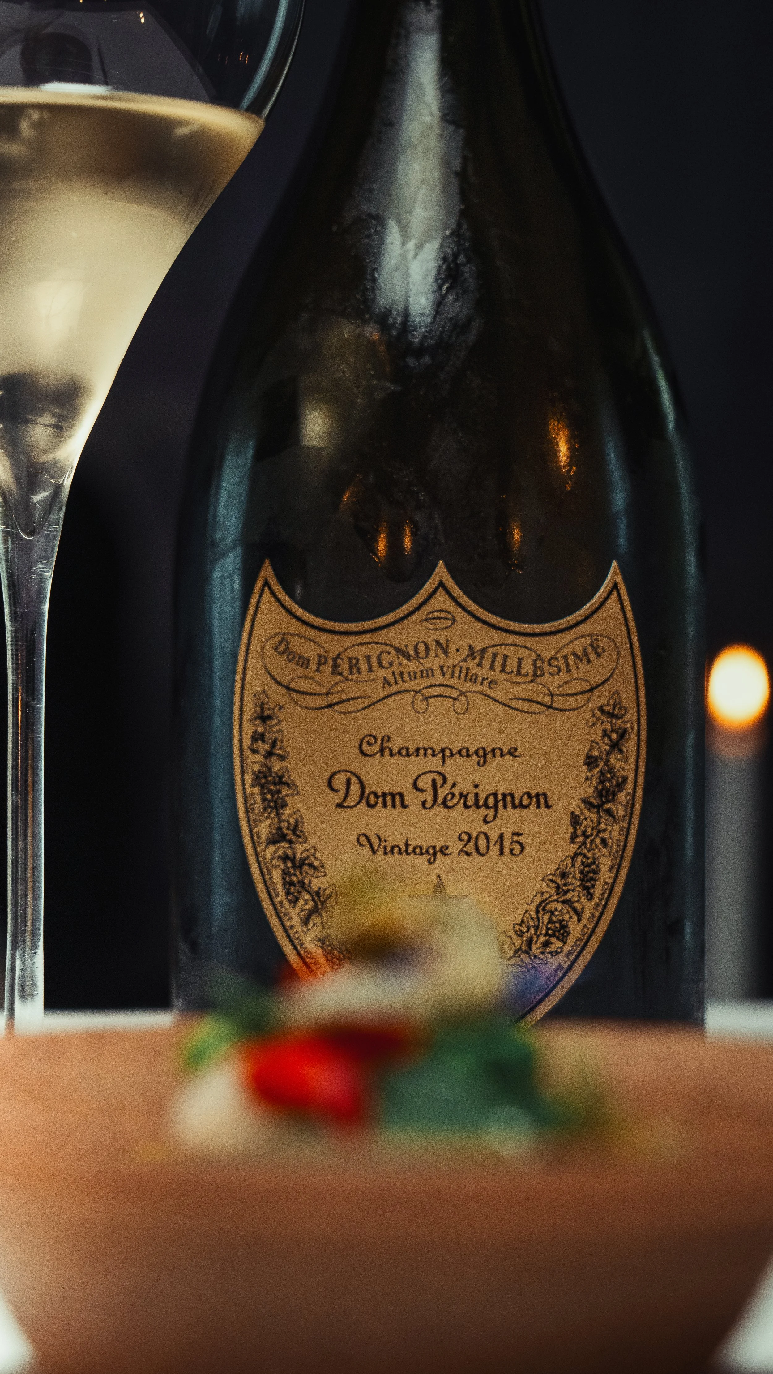 A bottle of Dom Pérignon vintage 2015 champagne next to a filled champagne flute.