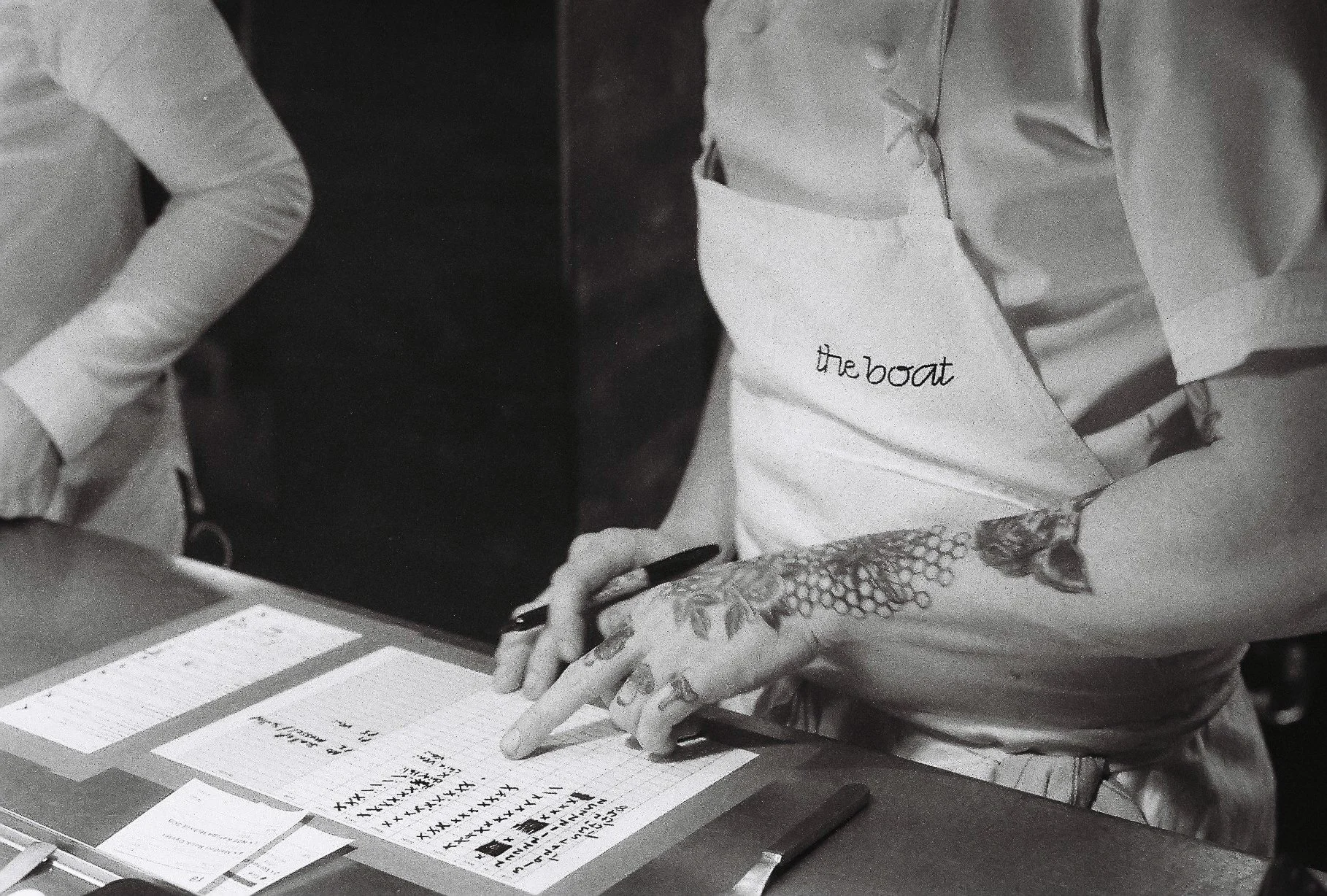 People wearing white lab coats and protective gloves working with papers, documents, and charts on a desk in a laboratory or office setting.