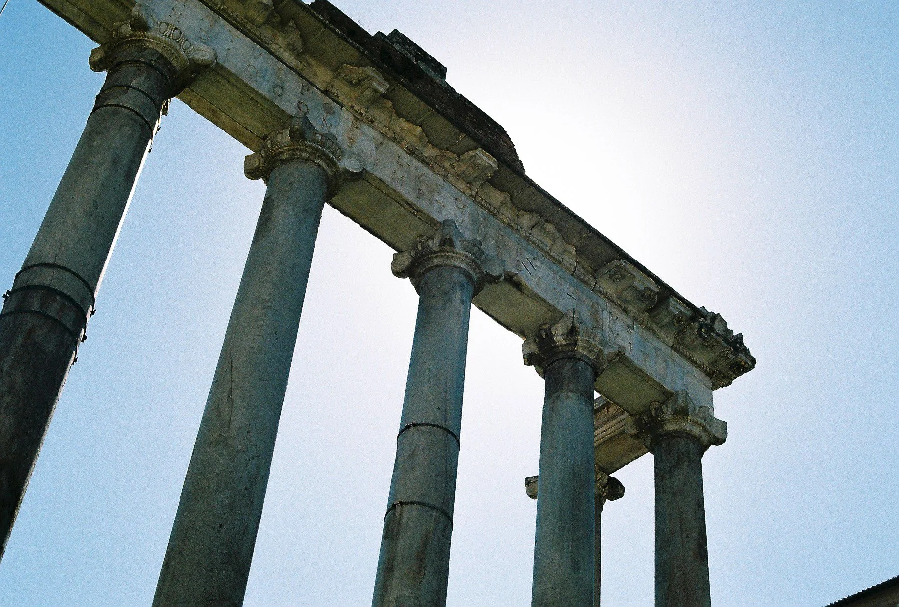 Ancient stone ruins with four large columns supporting a horizontal stone entablature, set against a clear sky.