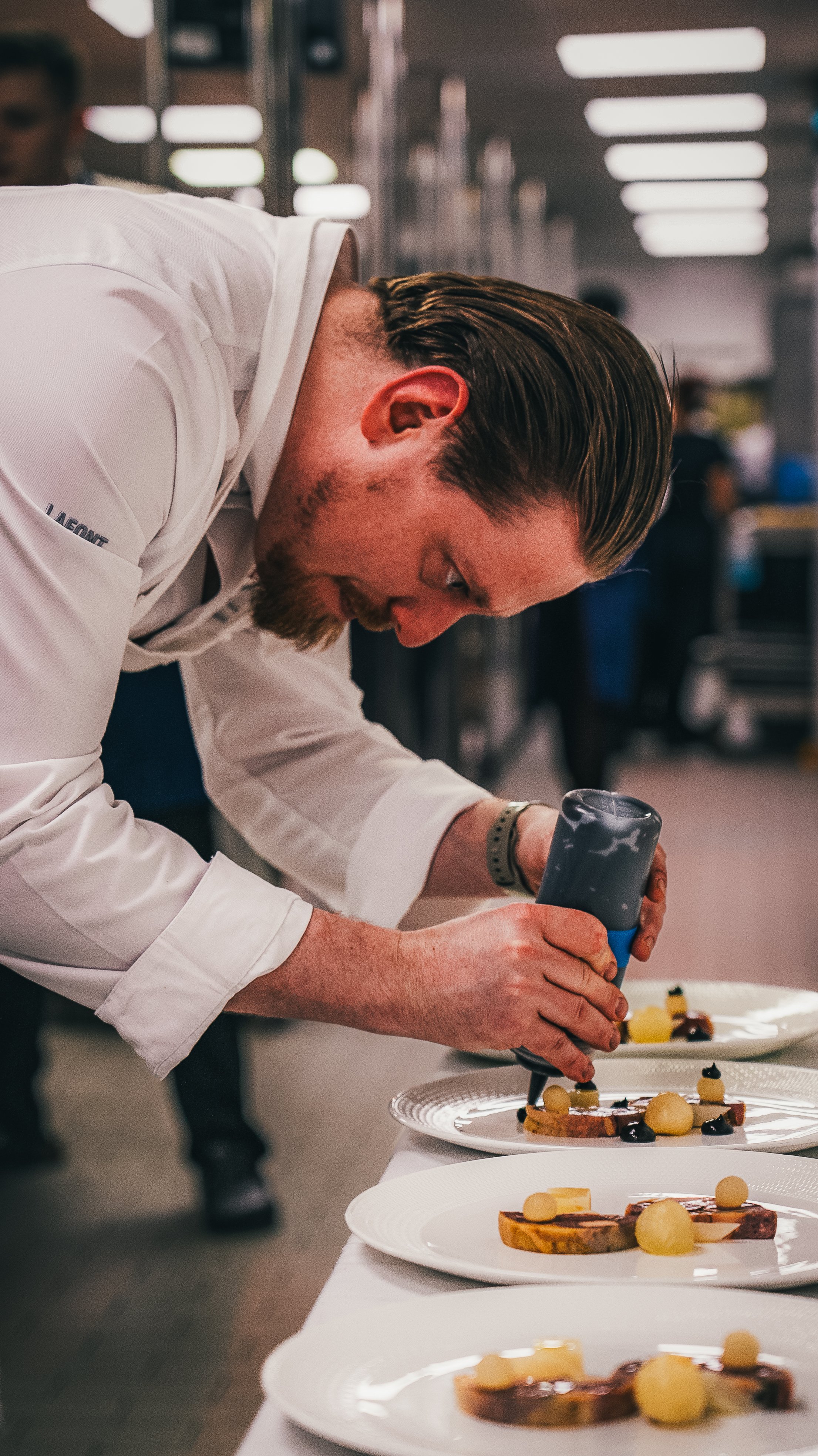 A chef garnishing plated desserts in a professional kitchen.