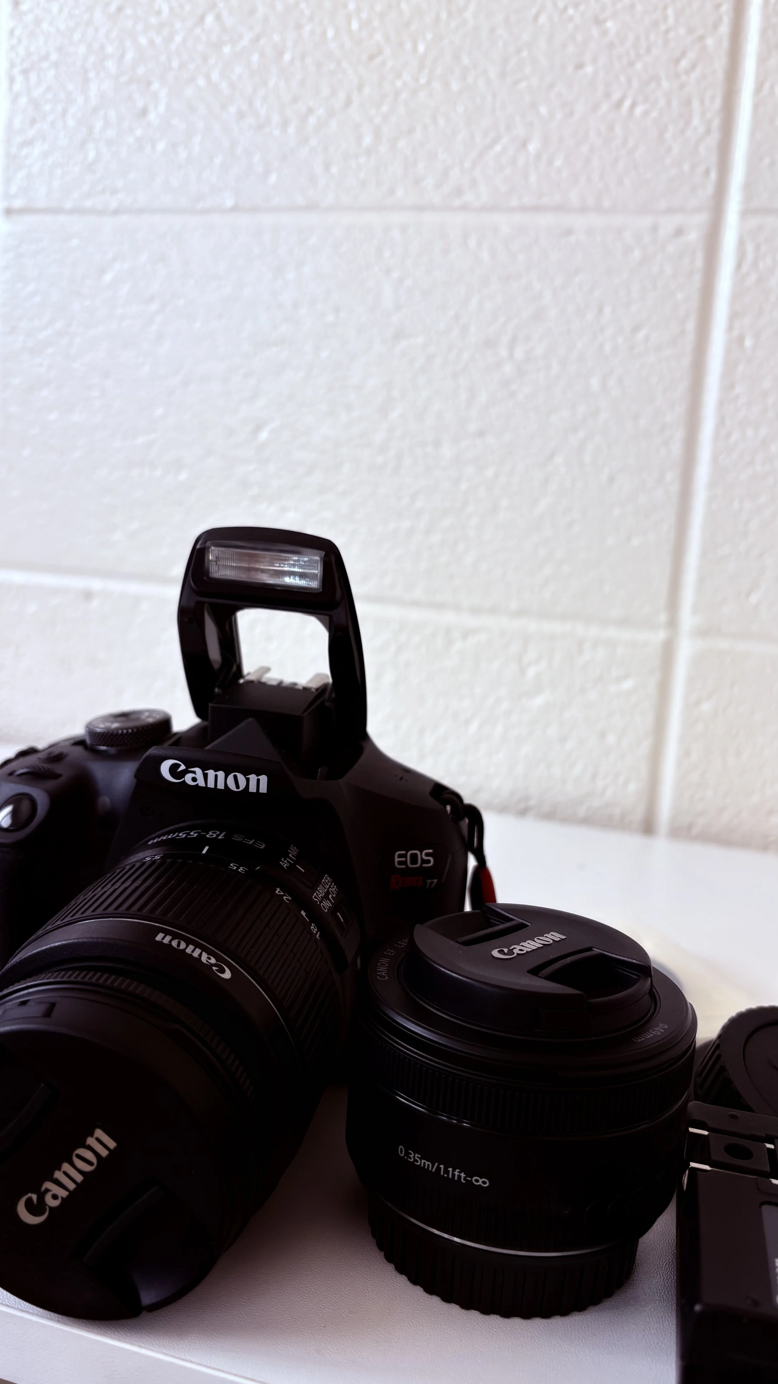 Canon camera with additional lens and a camera flash mounted on top, placed on a white surface.
