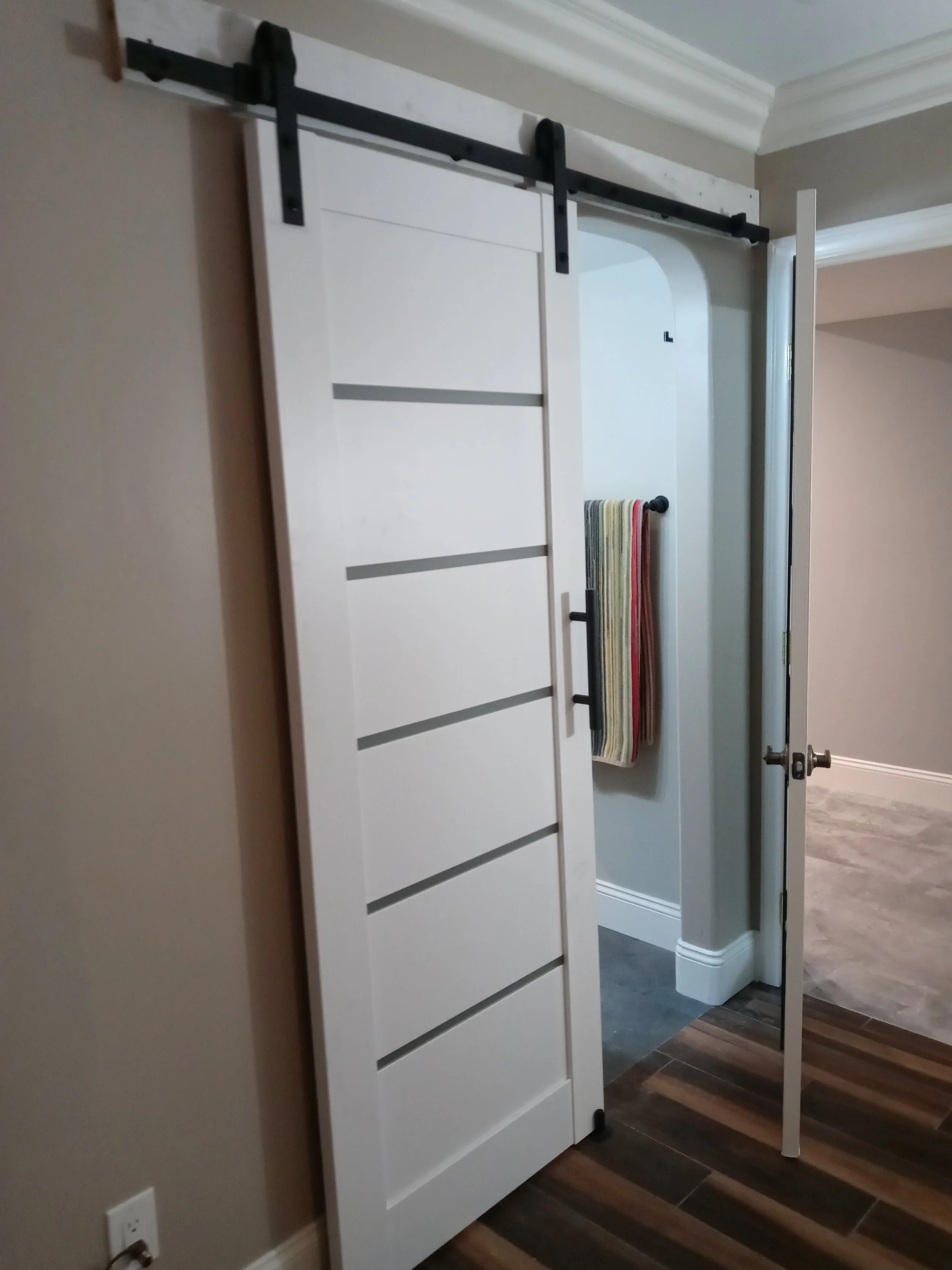 Sliding barn door with white panels and black hardware, partially open in a home interior.
