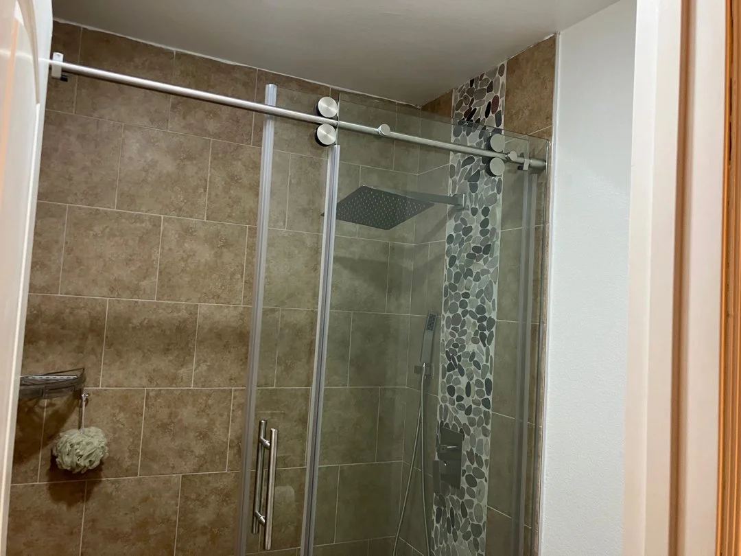 Bathroom shower with glass door, beige tile walls, and decorative pebble tile accent.