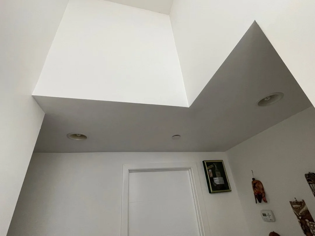 Ceiling with recessed lights, white walls, and wall decor including a framed picture, a small animal figurine, and hanging decorations.