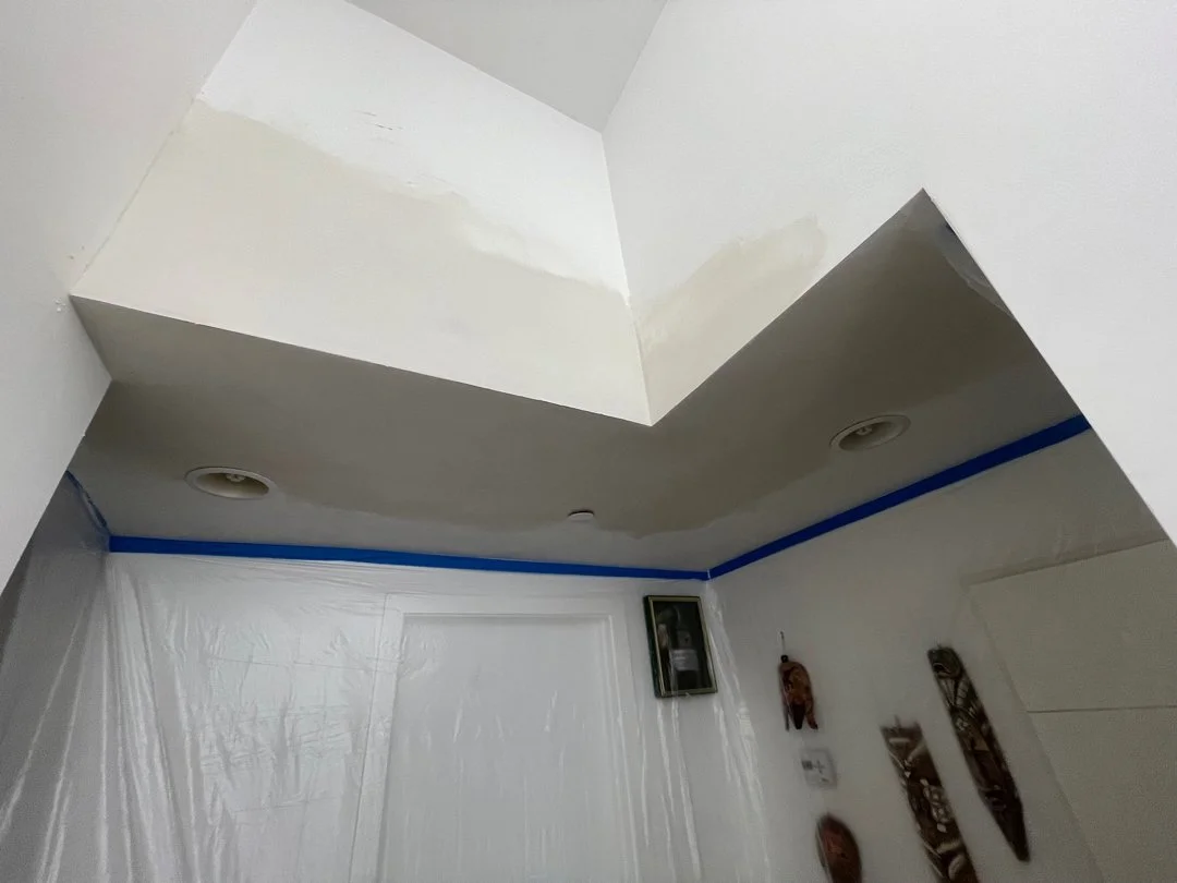 Ceiling with recessed lighting, blue painter's tape along the edges, and wall decorations including masks.