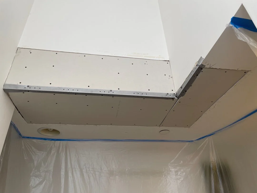 Ceiling installation with drywall panels and a cutout for a light fixture, plastic sheeting, and painter's tape.