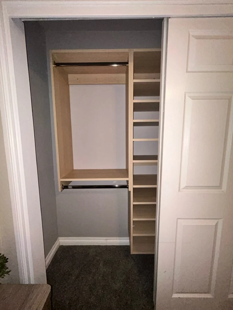 Empty closet with wooden shelves and hanging rods, inside a room with gray walls and white trim.