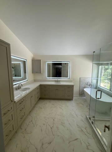 Modern bathroom with beige cabinetry, marble floor, a glass-enclosed bathtub, a double sink vanity, and two windows providing natural light.
