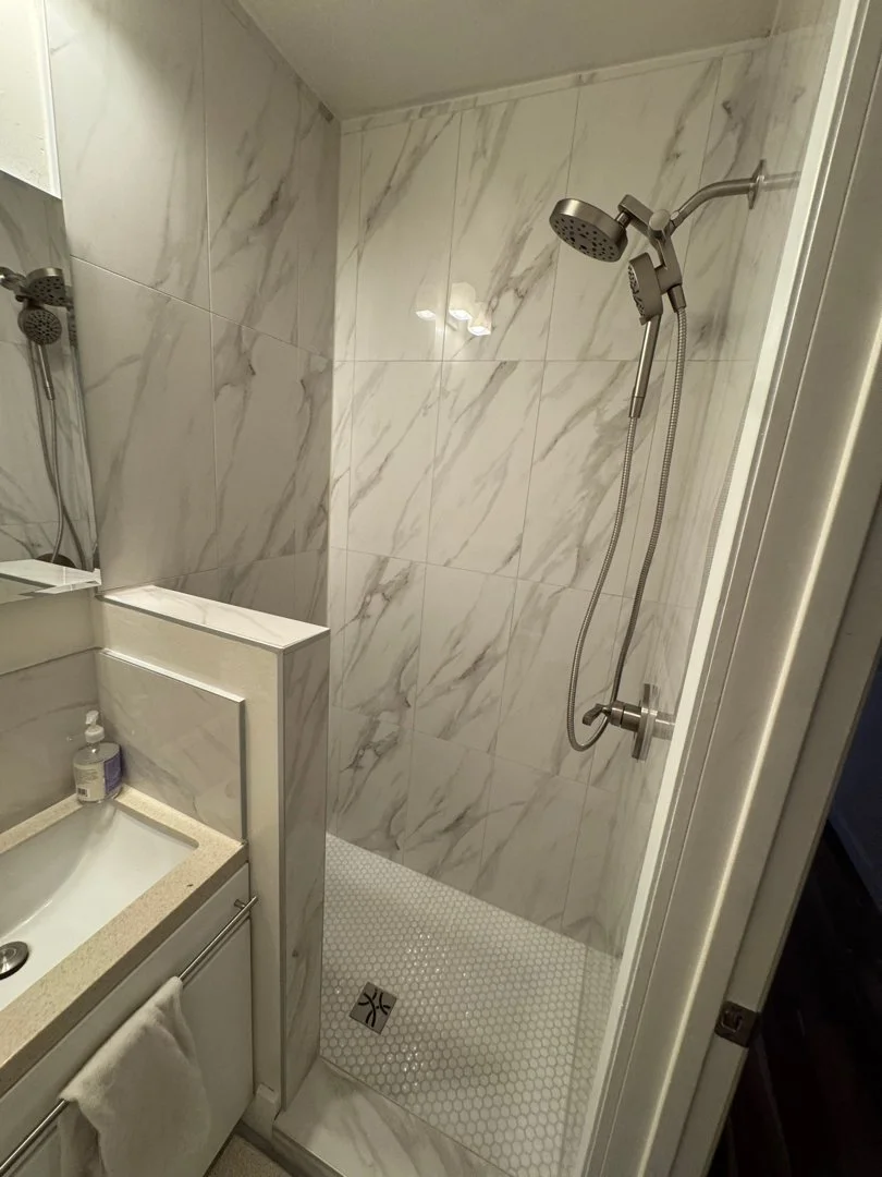 Shower area with marble tiles, a handheld shower head, and a small tiled shower floor with a drain.