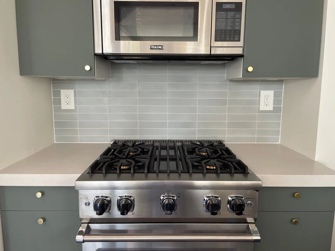 Stainless steel Viking microwave oven mounted above a gray gas stove with five burners, set in a white countertop with gray cabinets and a gray tiled backsplash.