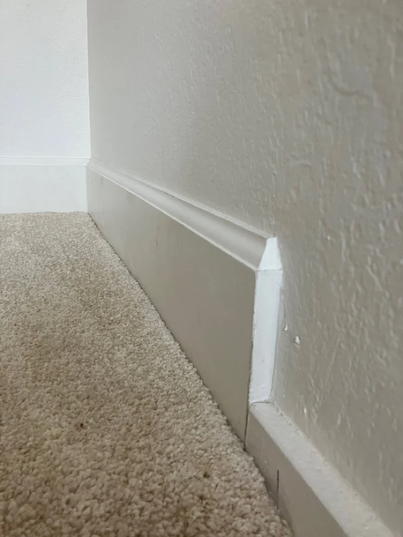Close-up of a beige carpeted floor and a white baseboard heater against a textured cream wall.