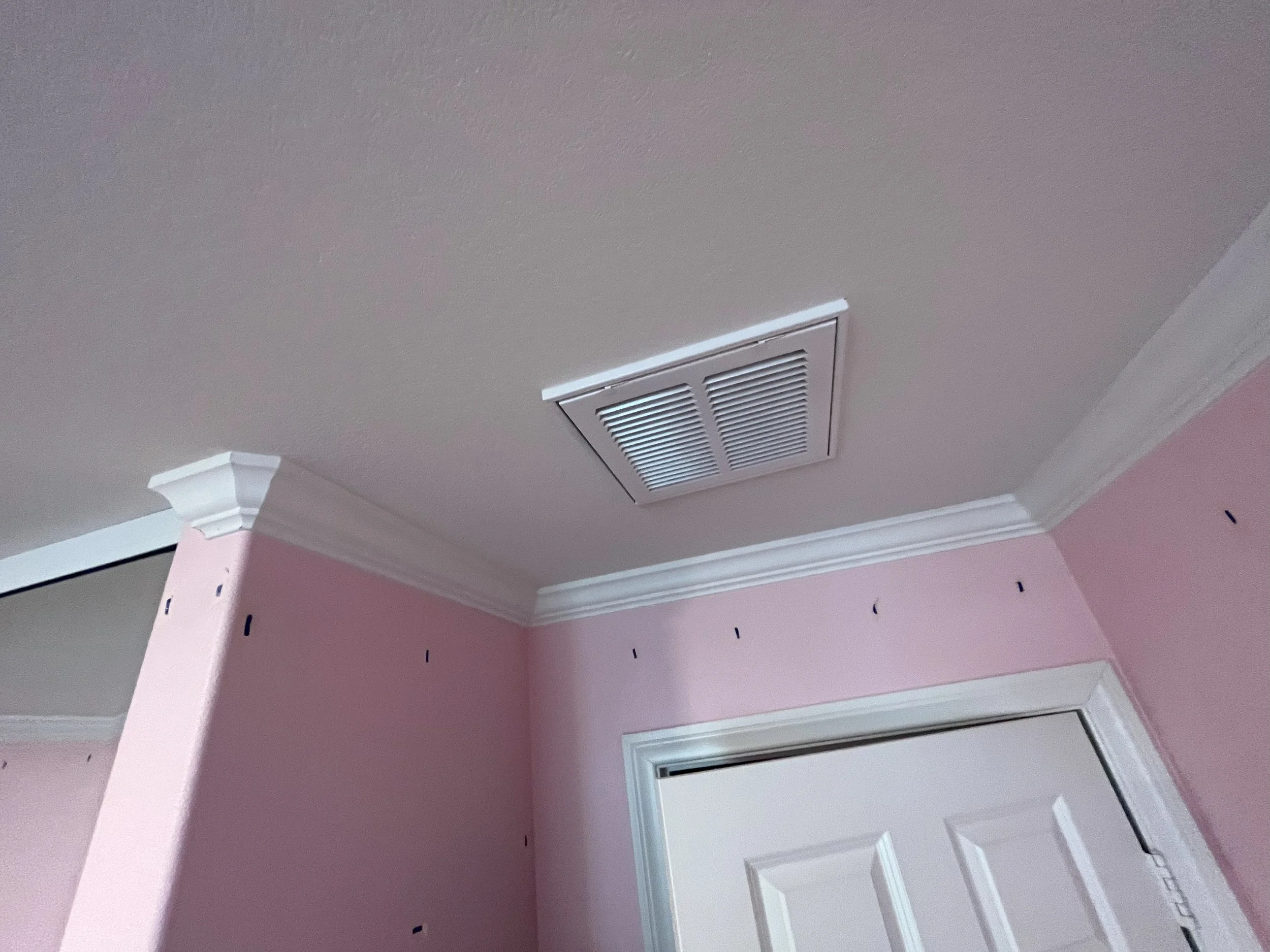 Ceiling vent in a room with pink walls, white crown molding, and a door.