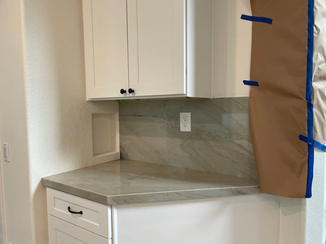 Kitchen countertop with white cabinets above, a power outlet on the wall, and a large piece of brown paper taped to the right side.