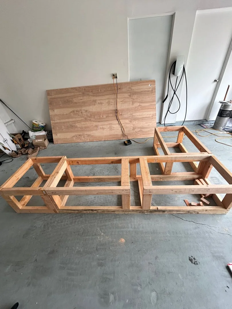 unfinished wooden bed frame on concrete floor in a room under construction with tools and materials nearby