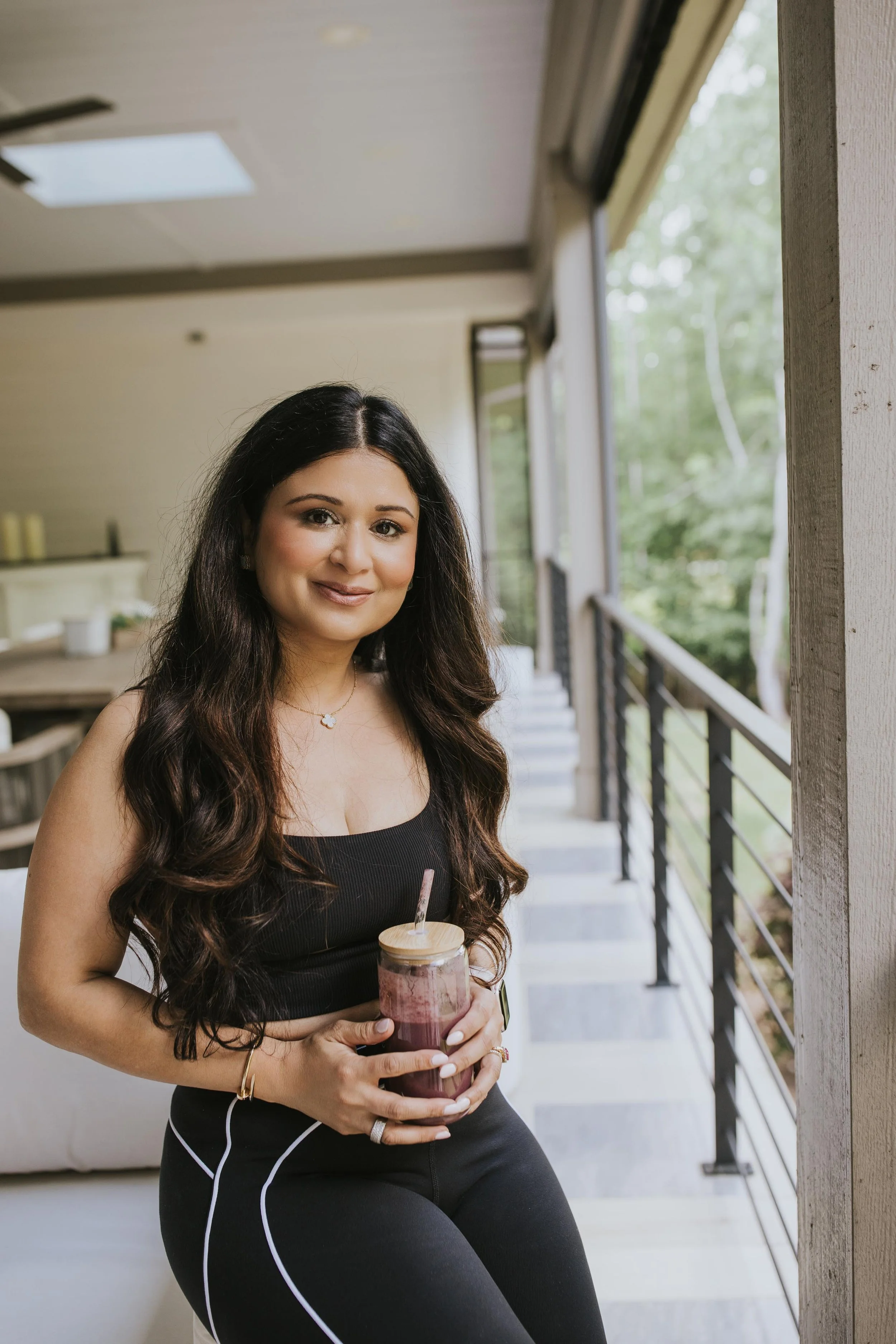 Dr. Sharma in workout gear, smiling in her home and holding a purple smoothie