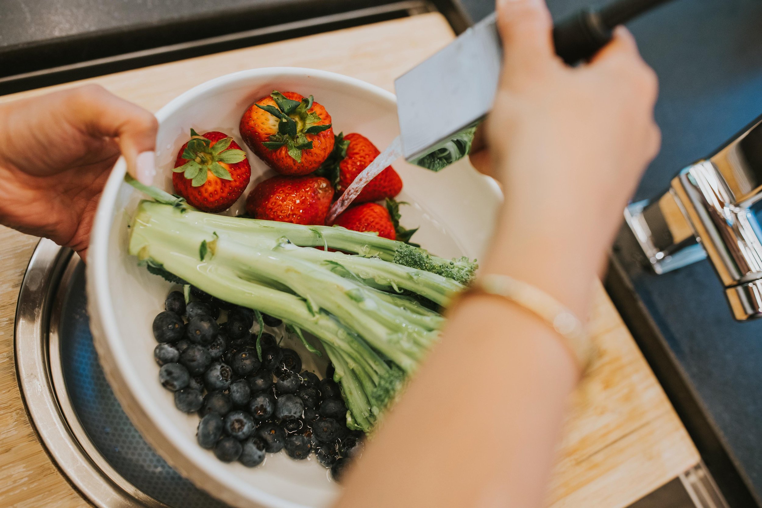 bowl of strawberries, blueberries, and greens getting rinsed
