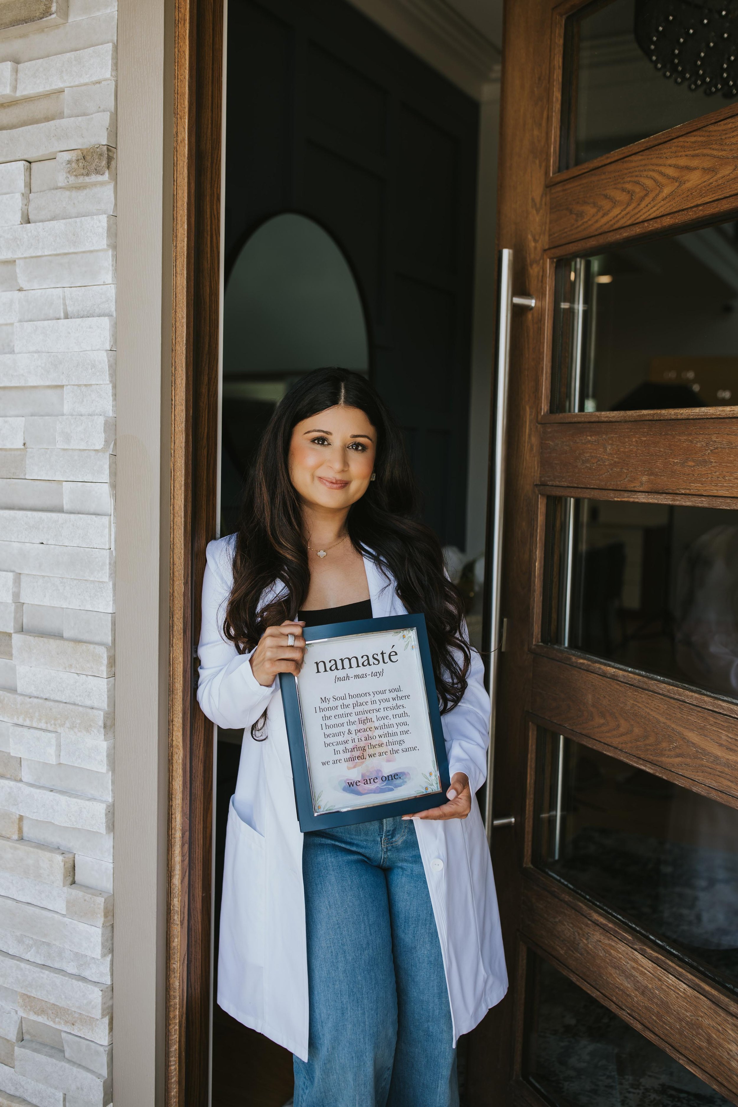Dr. Sharma smiling in front of an open door, holding a "namaste" sign