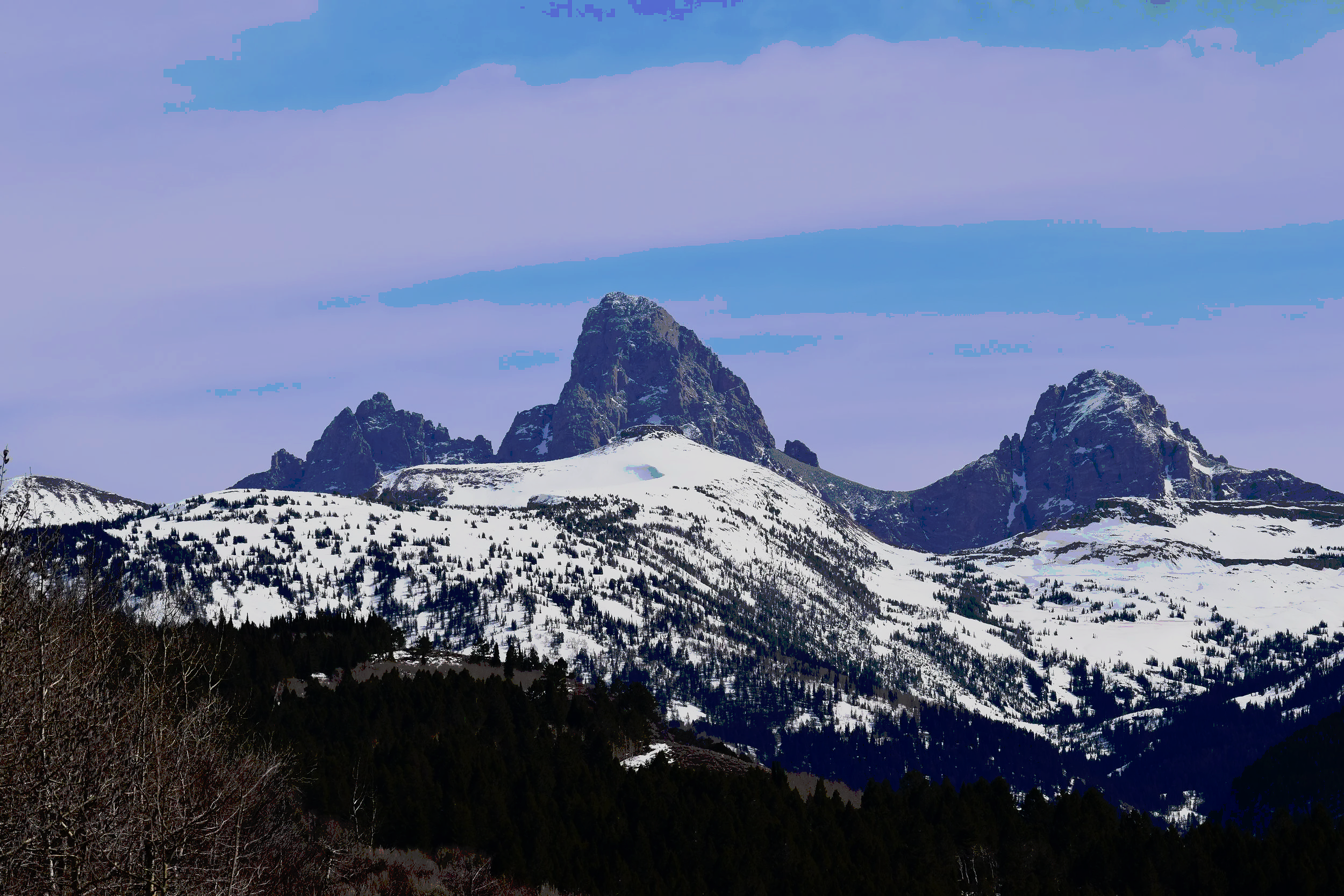 Snow-covered mountain range with prominent rocky peaks and a partly cloudy sky.